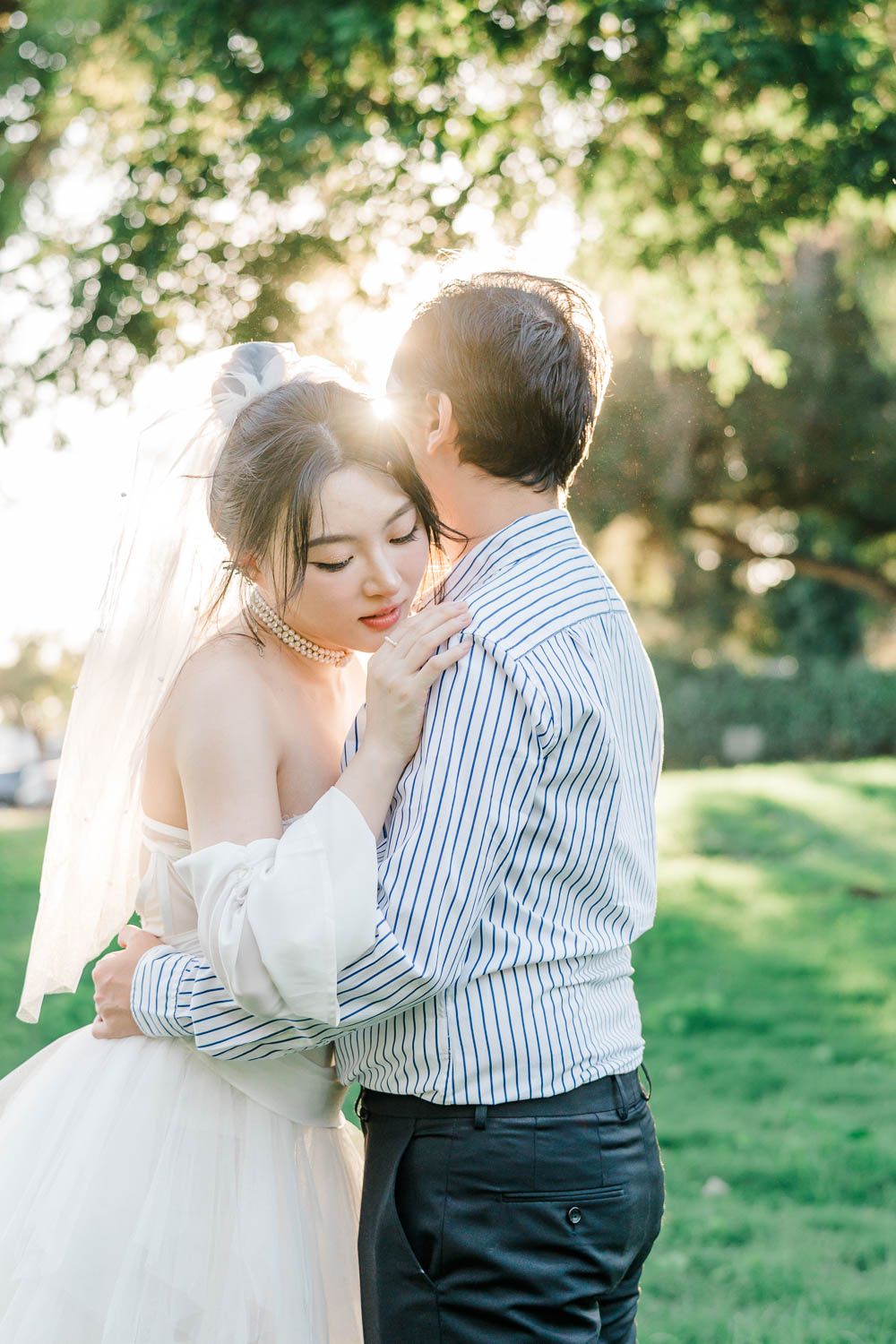 A romantic outdoor wedding photoshoot captures newlyweds embracing in a sun-dappled garden setting.