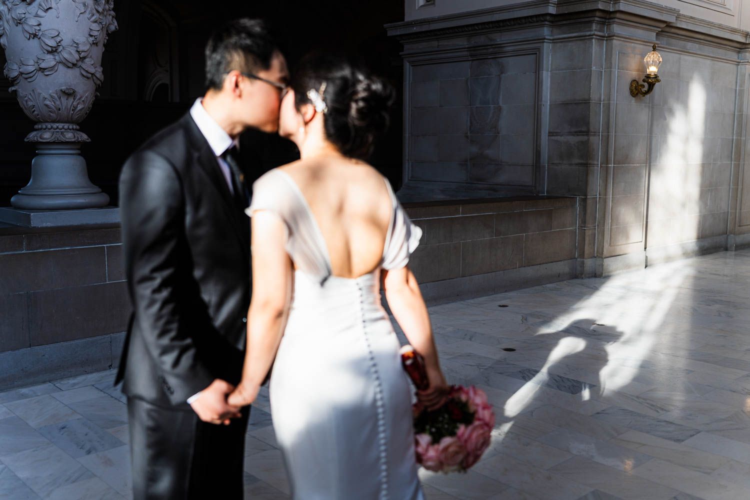 Two newlyweds share an intimate moment in formal attire outside an elegant stone building with dramatic lighting.