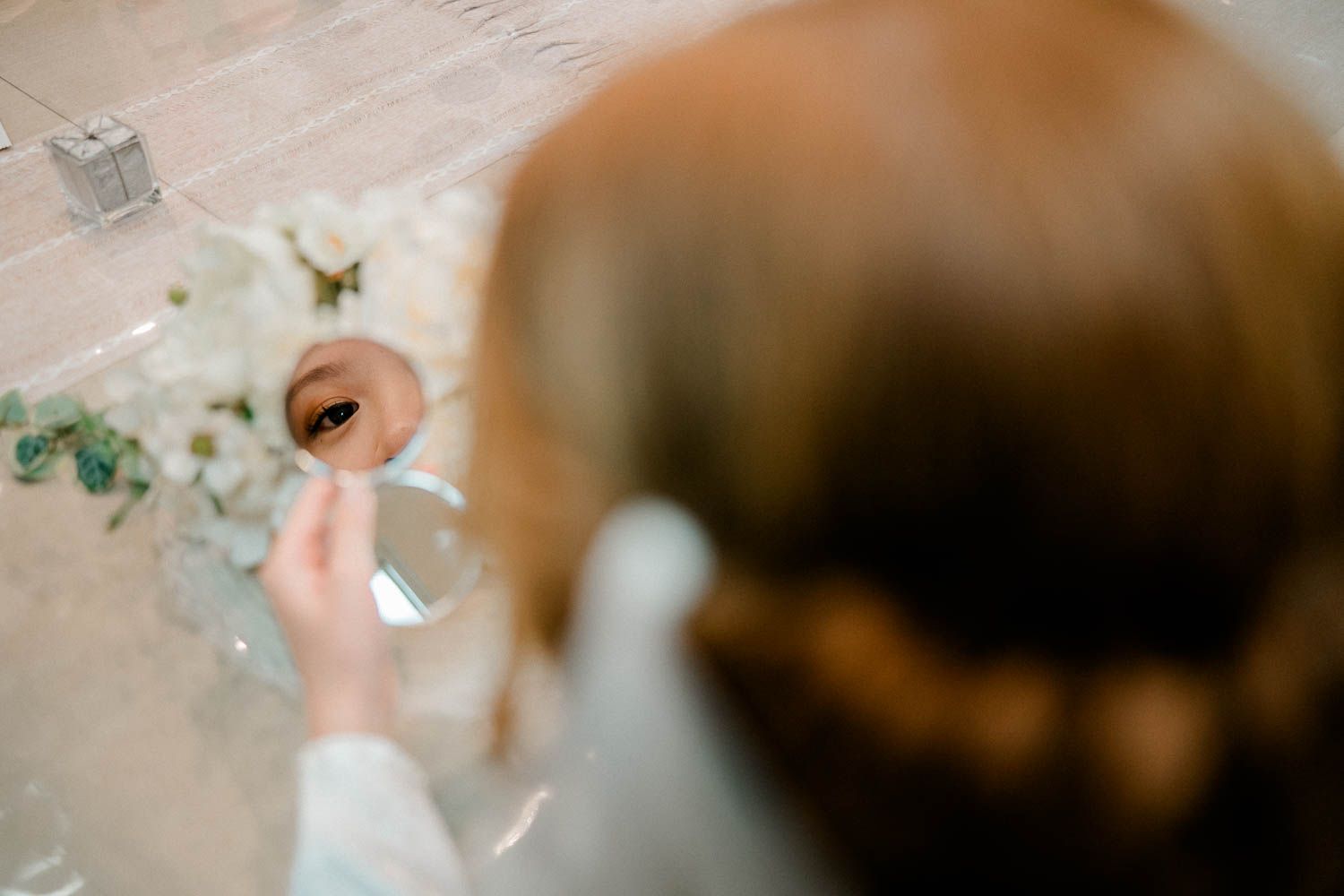 Above view of a bride holding a mirror with floral elements scattered around when getting ready for the ceremony.