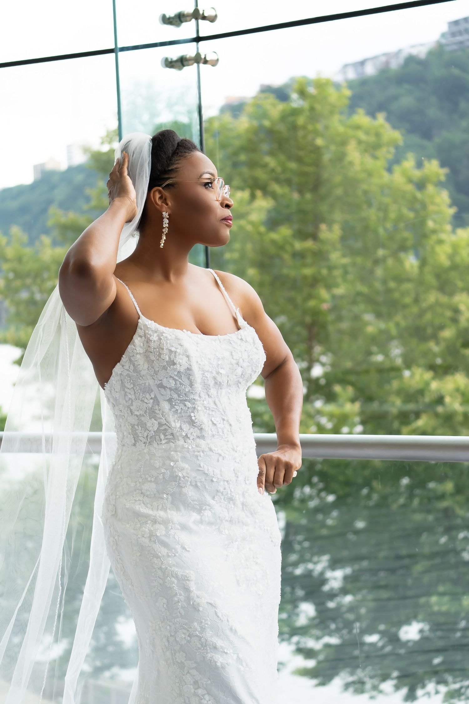 Beautiful African American bride in white lace wedding dress and flowing veil poses by window, Pittsburgh Pennsylvania. River Casino