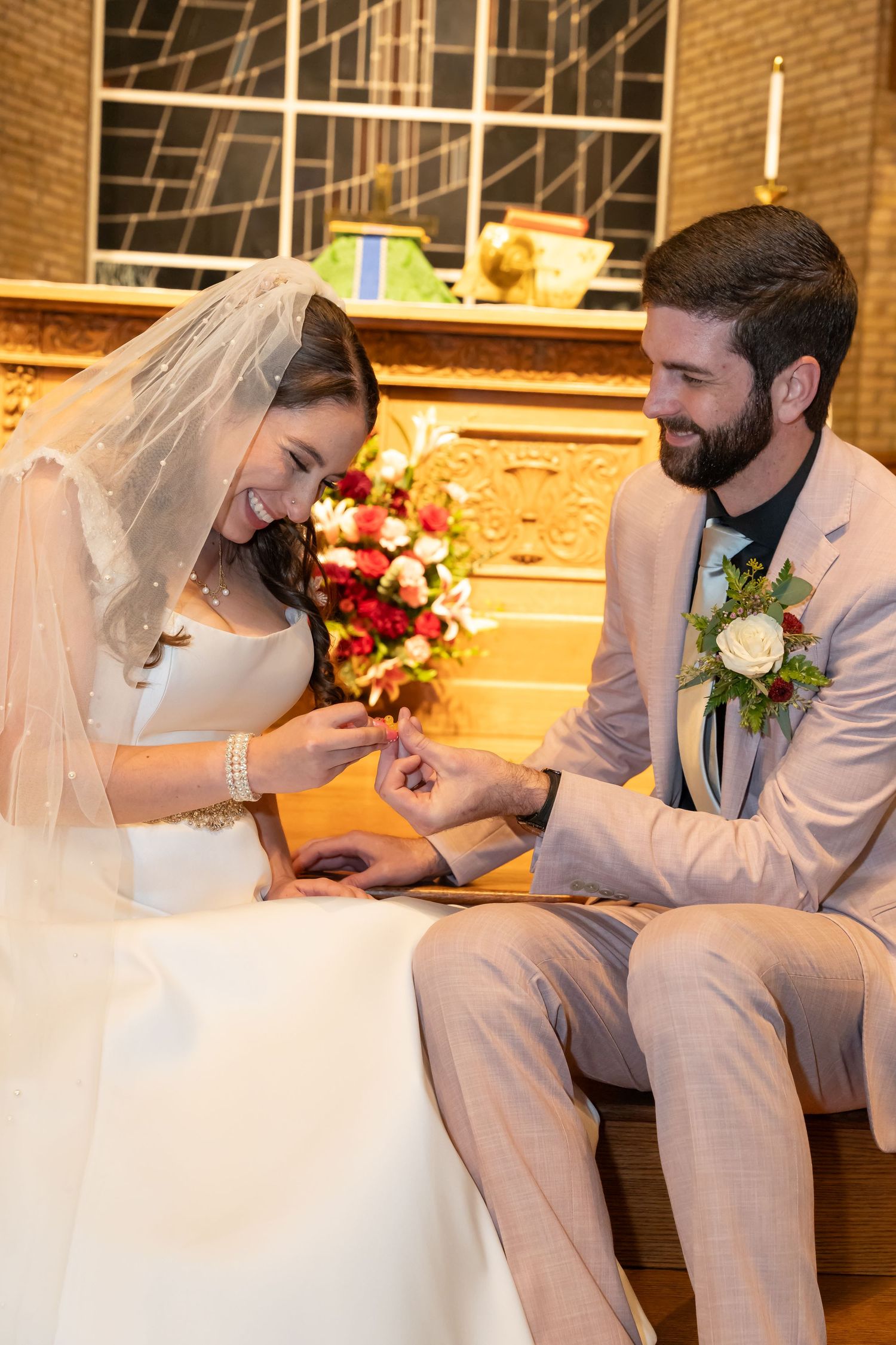 A couple shares a joyful moment during their wedding ceremony in a church with brick walls and floral decorations.  Vienna, Virginia