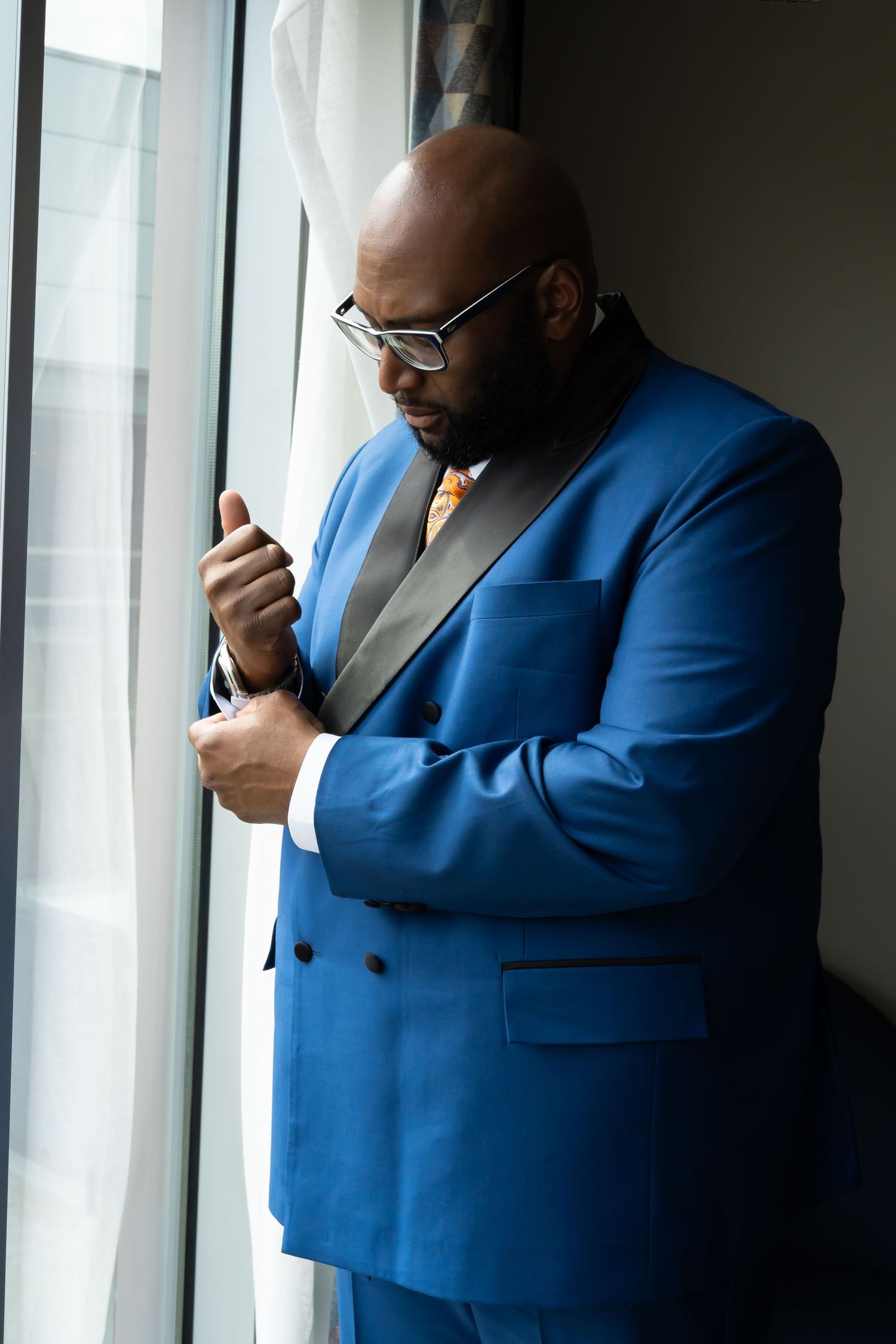 Groom in a bright blue suit stands by a window while looking down at wrist cuffs. Pittsburgh Pennsylvania River Casino