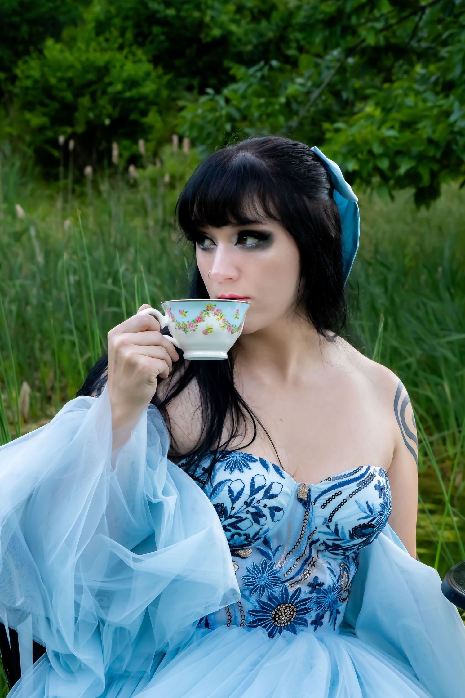 A series of photos showing someone in a light blue ethereal gown with dark hair drinking from a teacup in a garden setting.