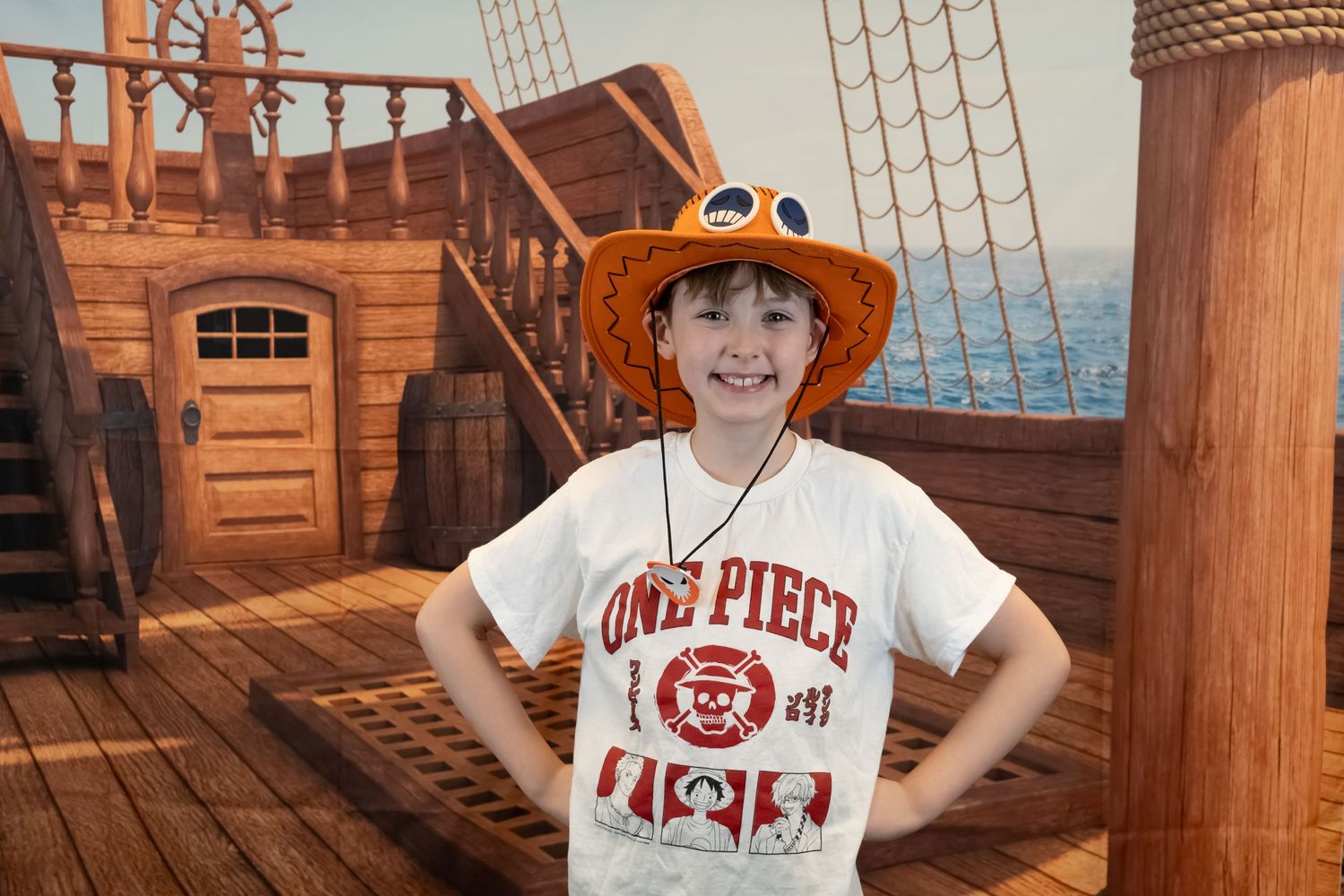 Young pirate enthusiast on a play ship deck wearing an orange hat and One Piece t-shirt.