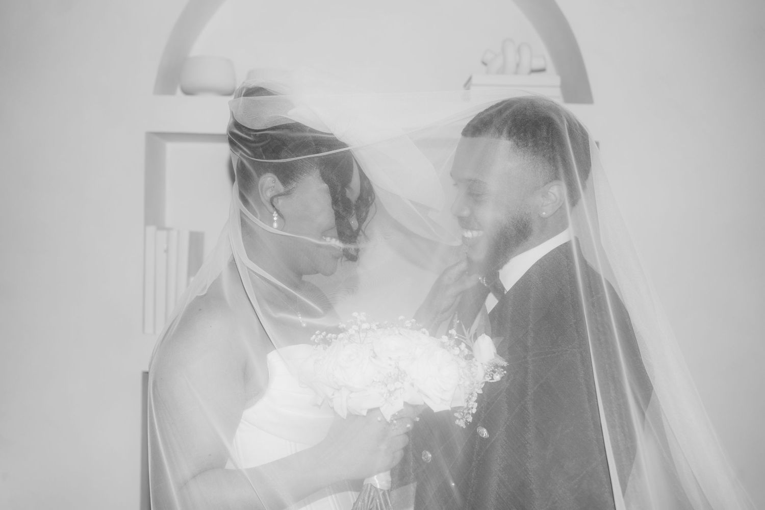 Black and white wedding photo of bride and groom sharing intimate moment under veil.