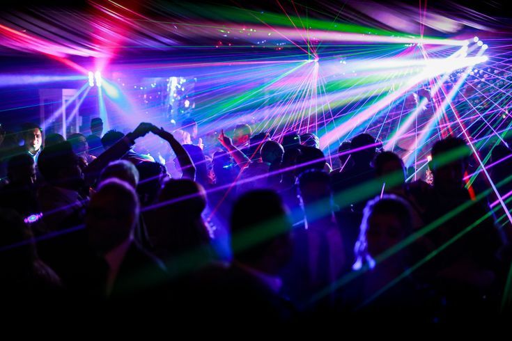 Crowd dancing under vibrant laser light show at a nightclub concert event.