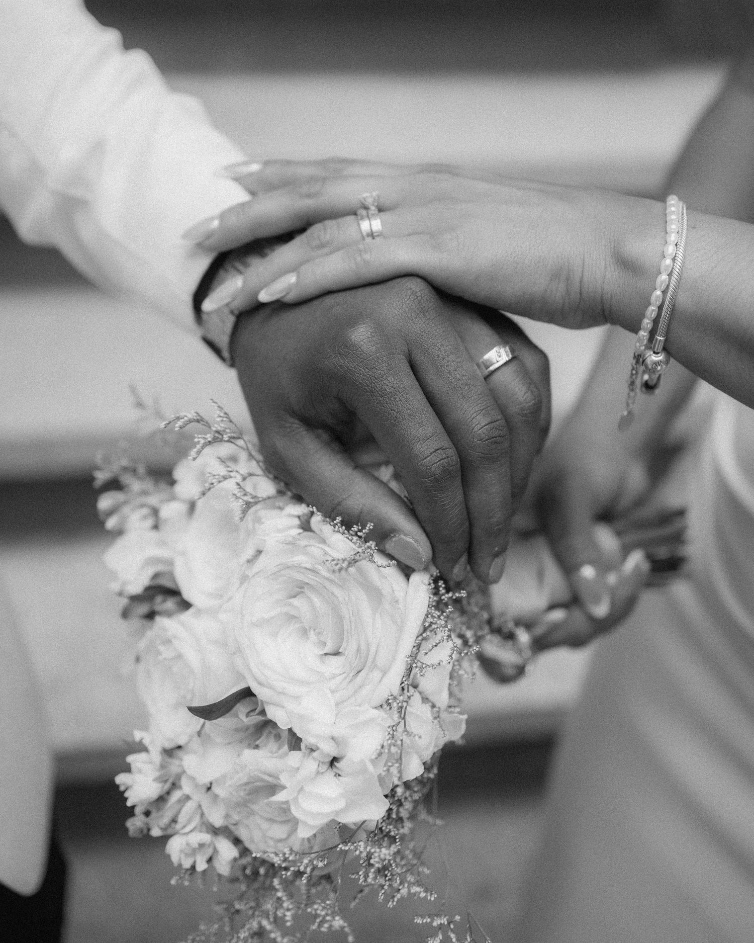 Black and white wedding photo of couple holding hands with rings and bridal bouquet of white roses.