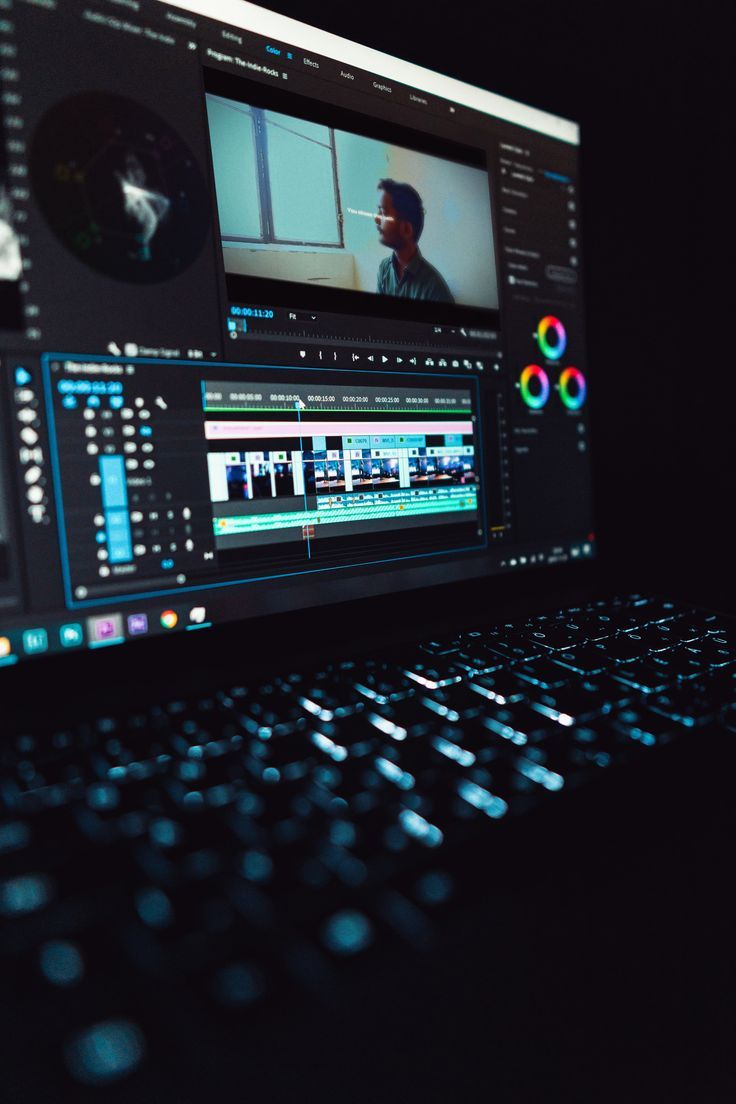 Laptop displaying Adobe Premiere Pro video editing software with timeline and color grading tools in dark room.
