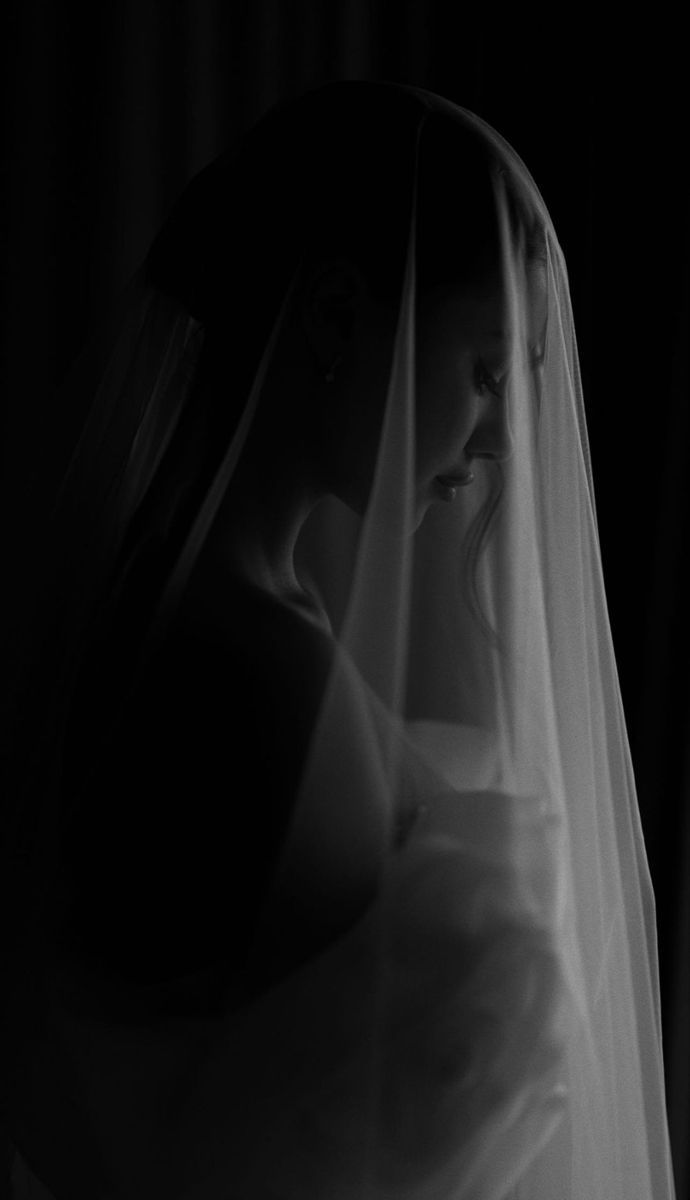 Black and white bridal portrait of a bride wearing a flowing veil in dramatic low-key lighting.