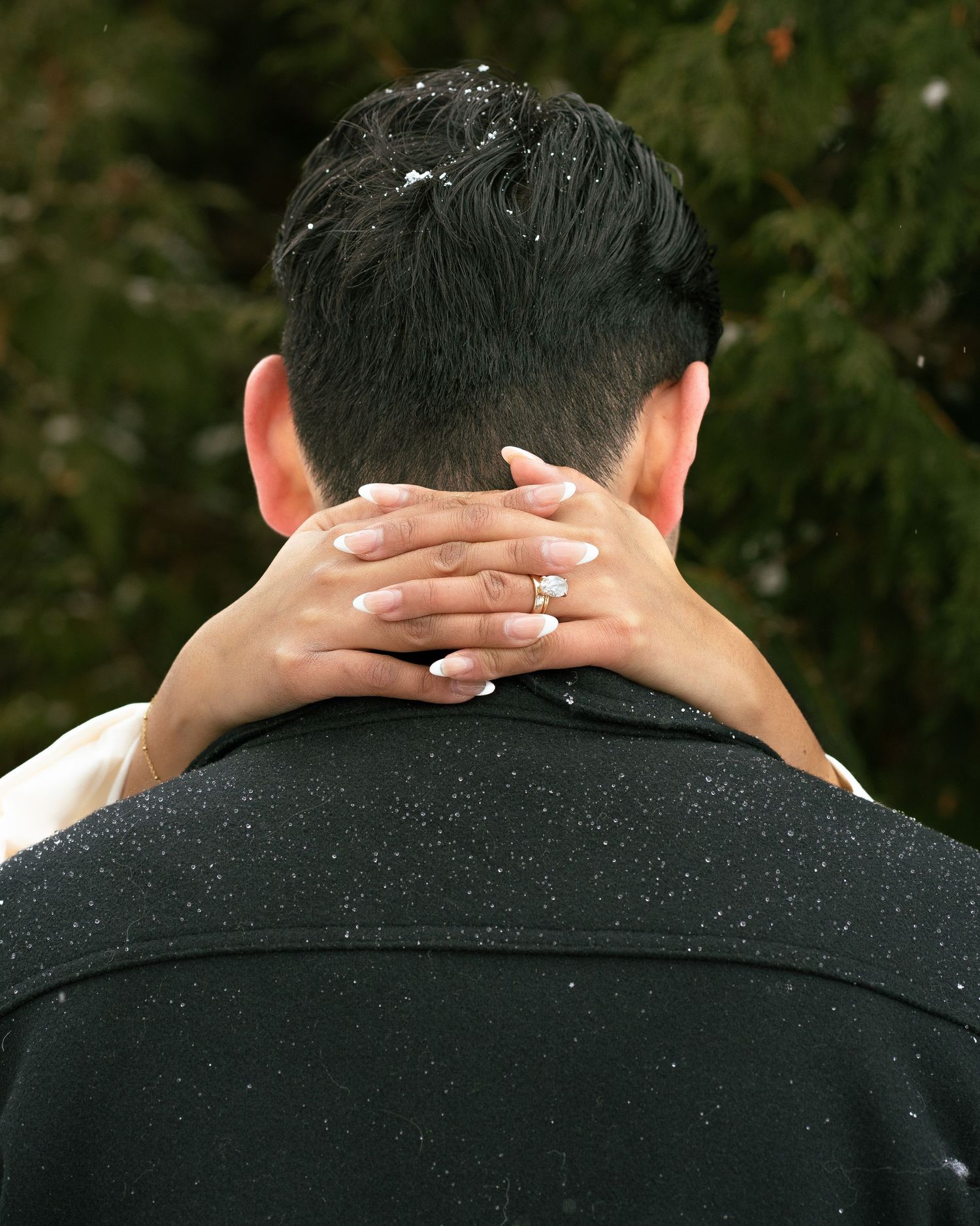 A person places their hand on the back of a man's neck during a snowy outdoor wedding ceremony.