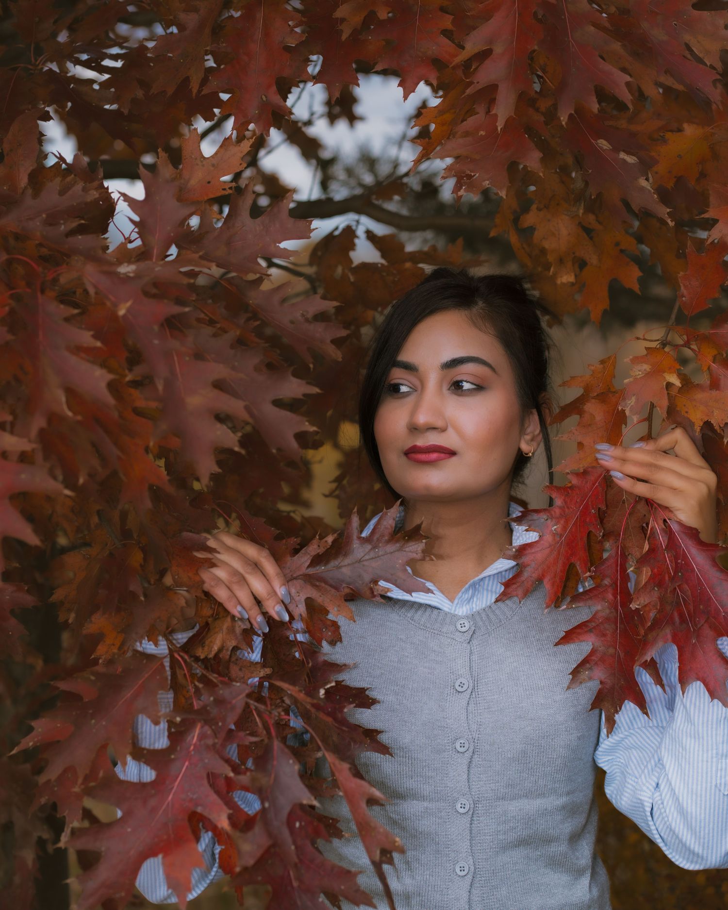 Autumn portrait with red maple leaves and grey sweater outfit.