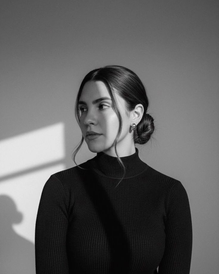 Black and white portrait of a young woman in a ribbed turtleneck with hair in a bun, soft shadow lighting.