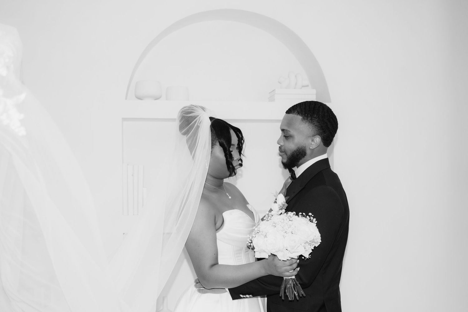 Black and white wedding photo of bride and groom sharing an intimate moment, bride holding white bouquet in elegant church.