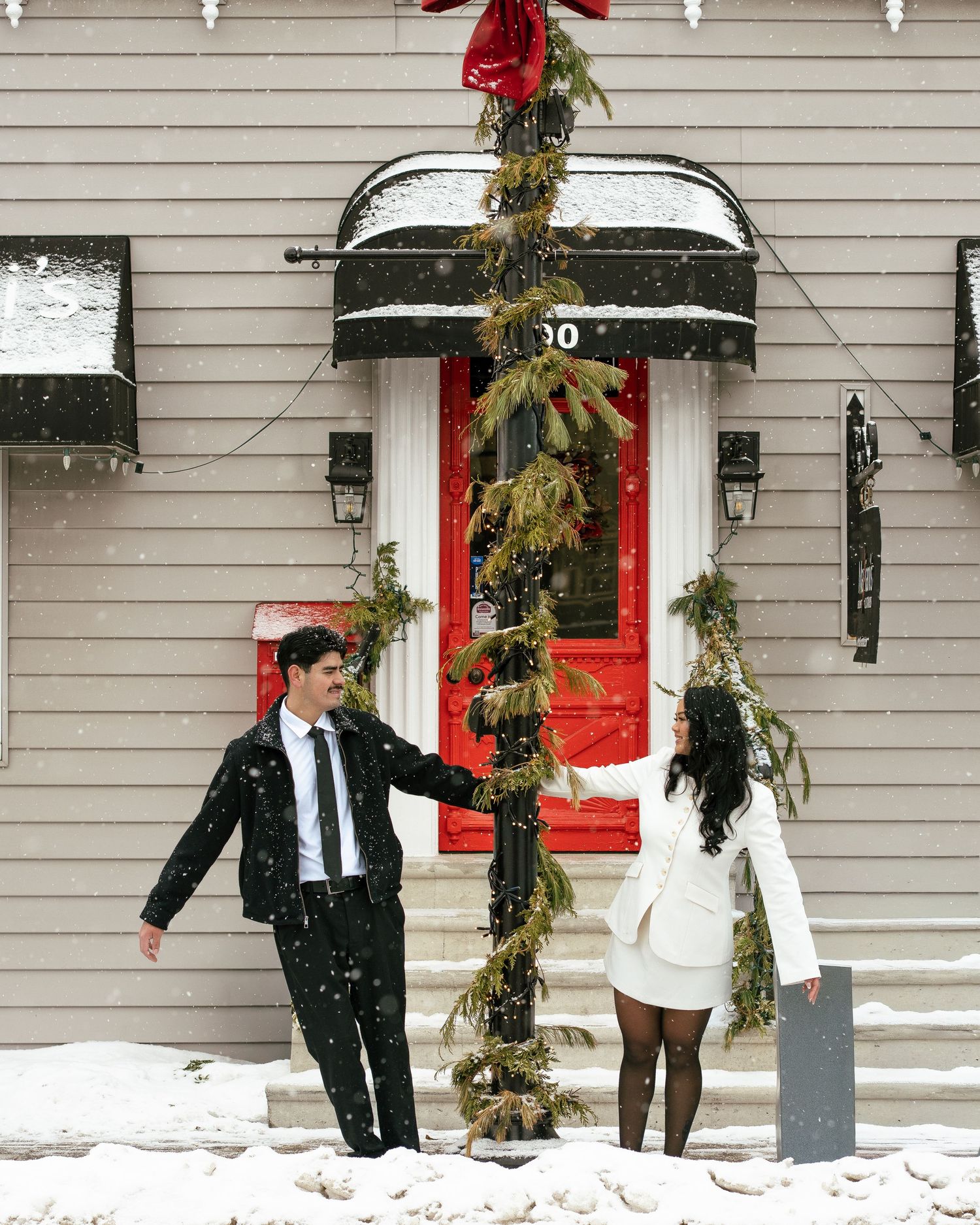 Winter wedding photo series outside a house with red doors and snow on the ground.