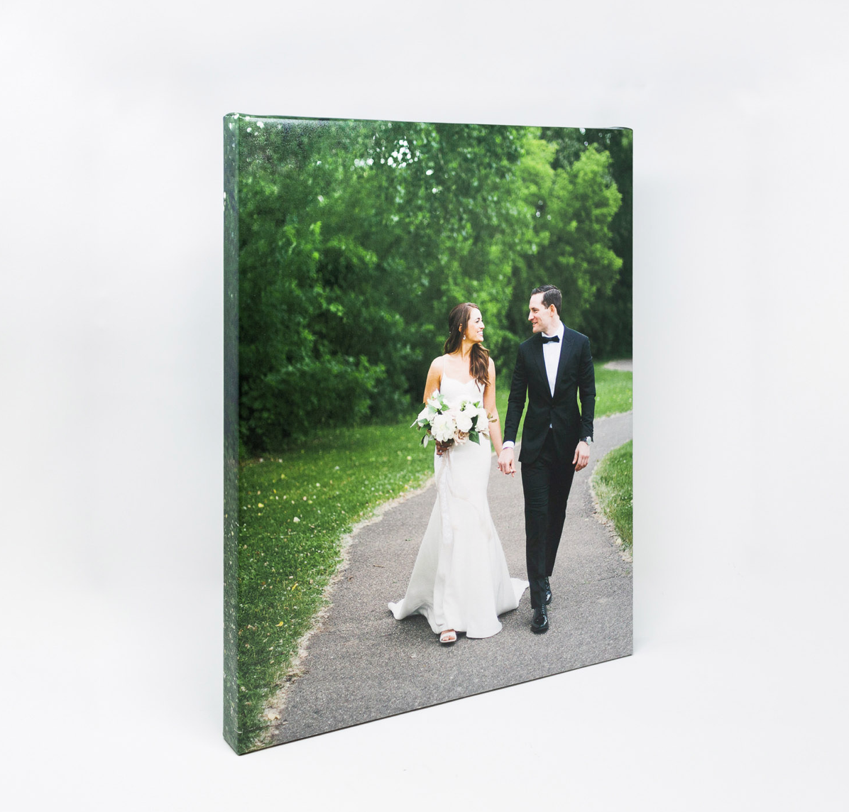 A couple in wedding attire walking together on a tree-lined path during a summer outdoor photo session.