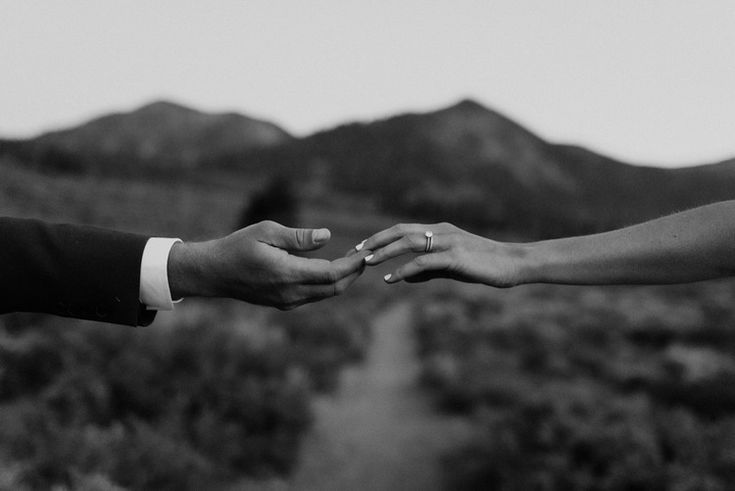 Black and white photo of couple holding hands with mountain landscape, bride wearing engagement ring.