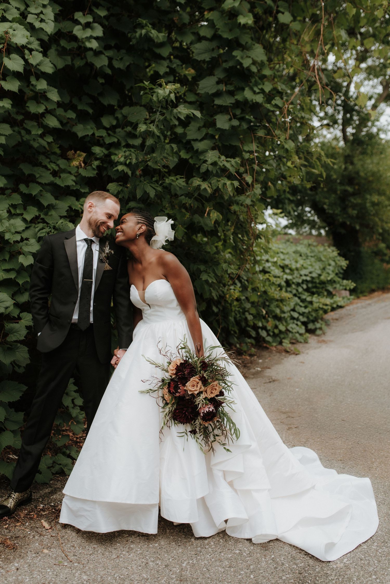 Two people in elegant wedding attire embracing on a garden path.