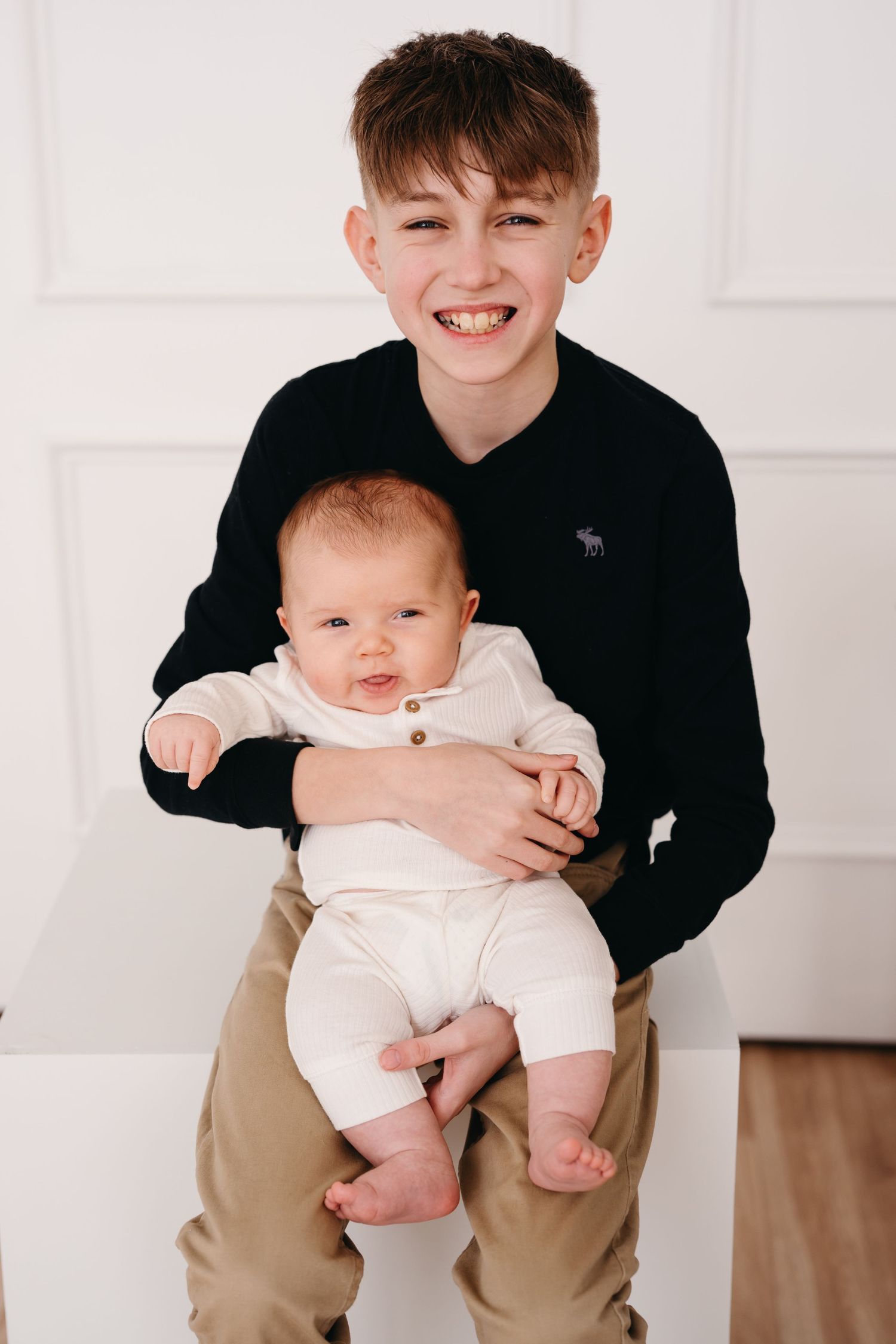 Young person in a black sweater holding a smiling baby wearing white clothing.