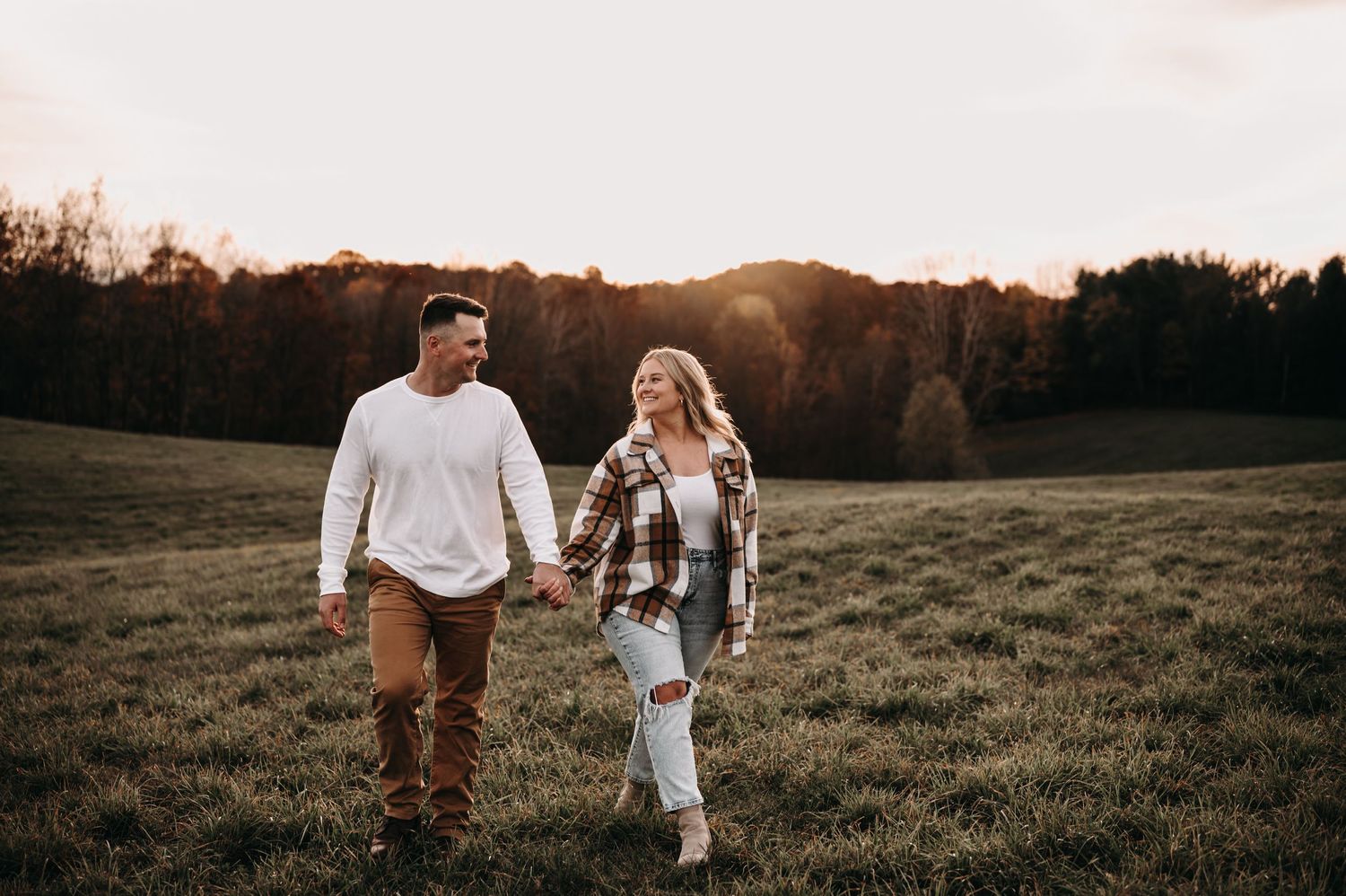 Couple walking hand in hand through autumn field at sunset.