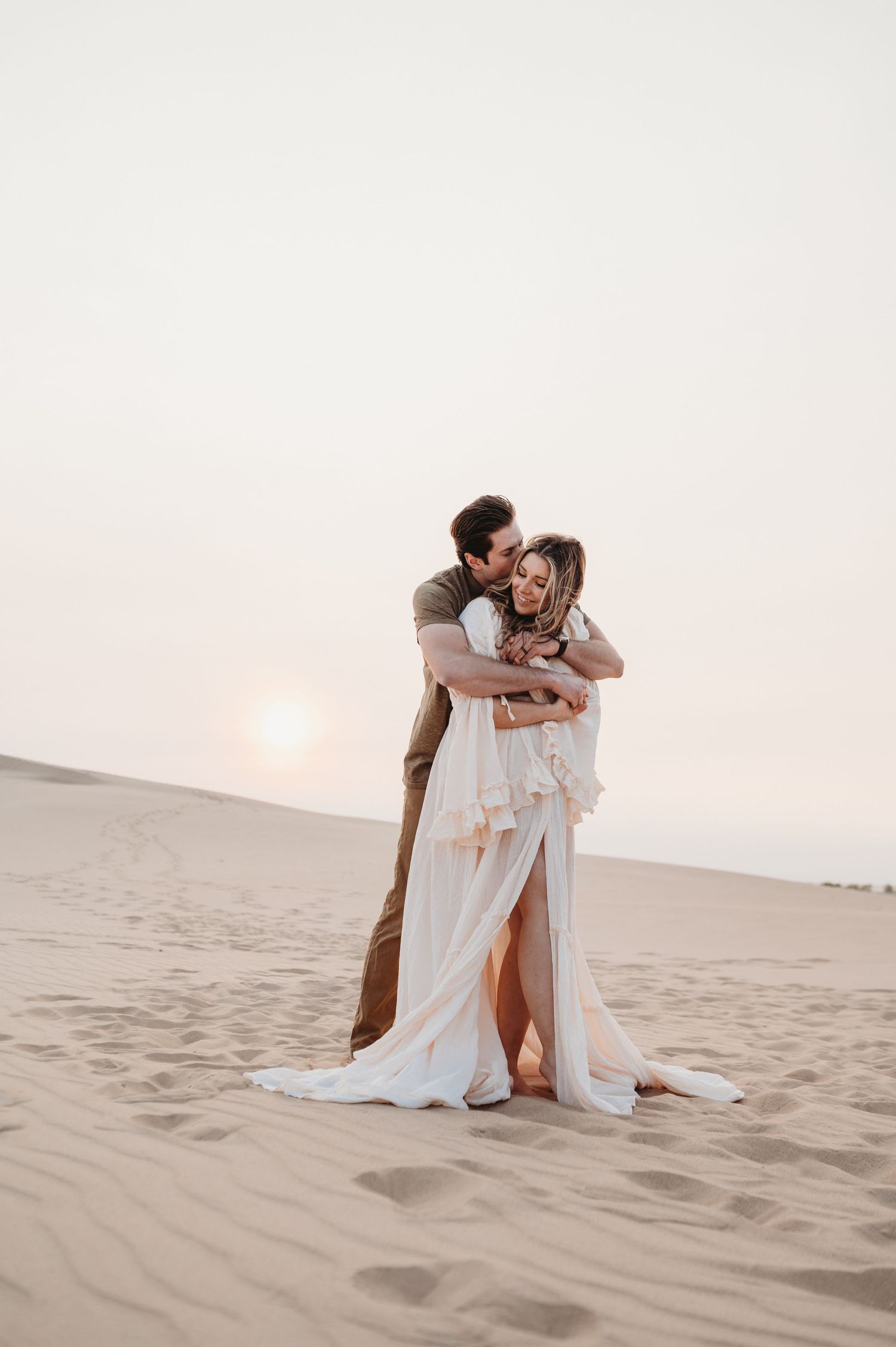 A loving embrace captured on desert sand dunes during golden hour.