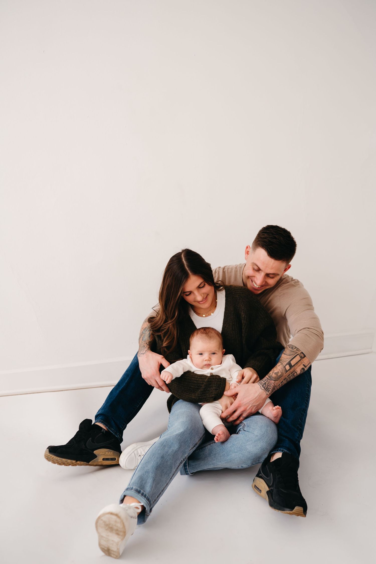 A family sits together on the floor sharing a tender moment with their baby against a white background.