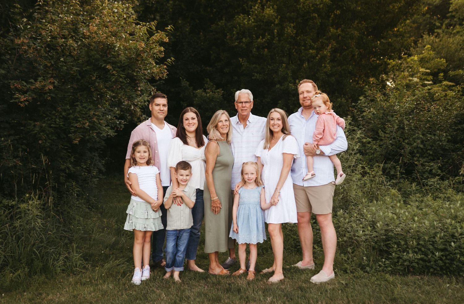 Multiple families posed together for portraits in a lush outdoor setting.