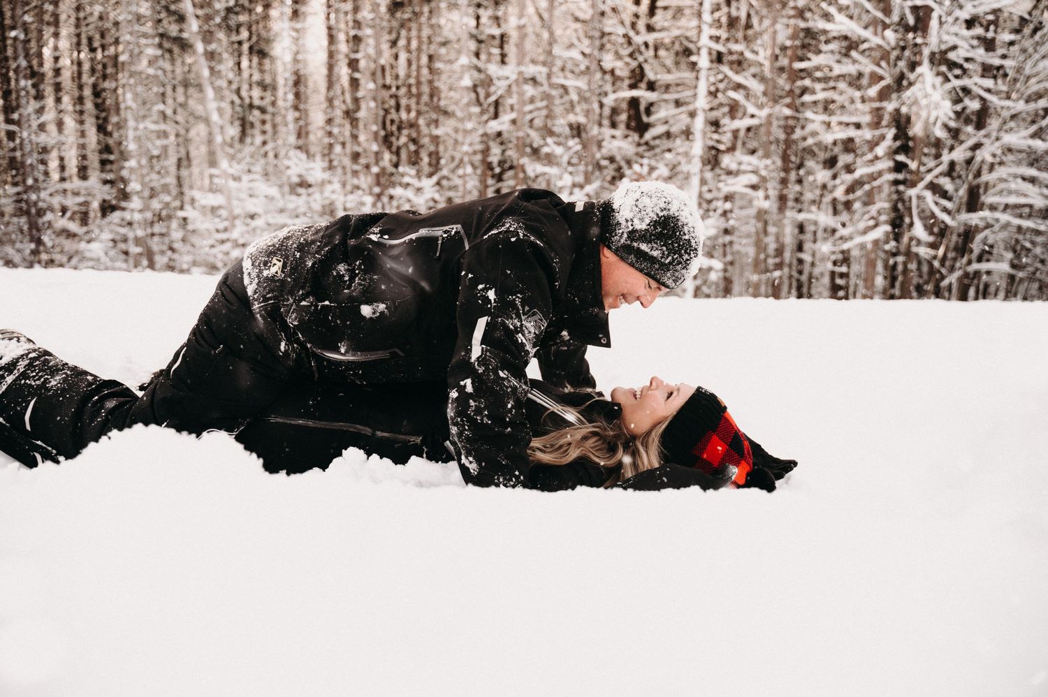 Two people in dark winter clothing share a moment in deep snow.