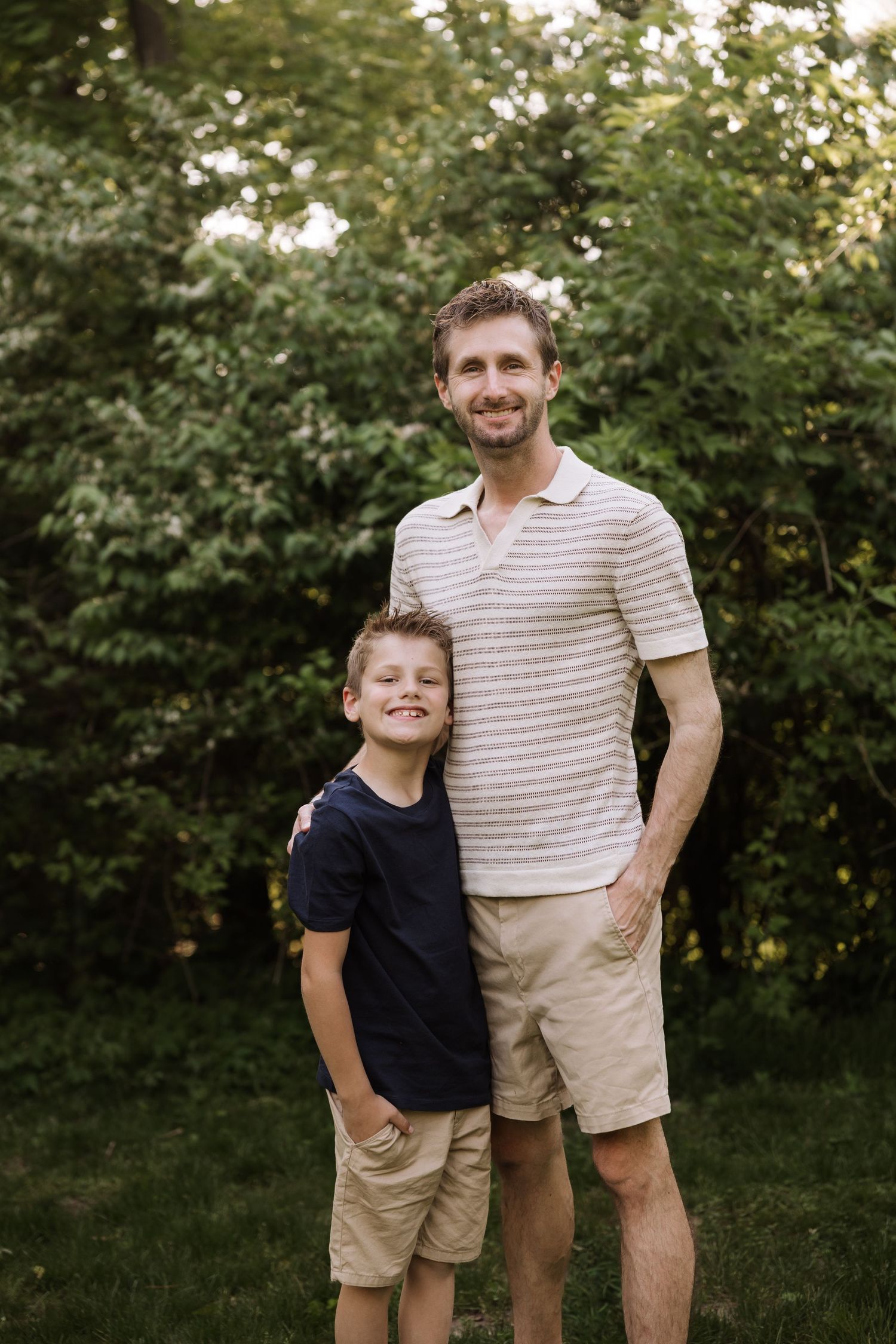 Smiling father and young son pose together in a lush green outdoor setting.