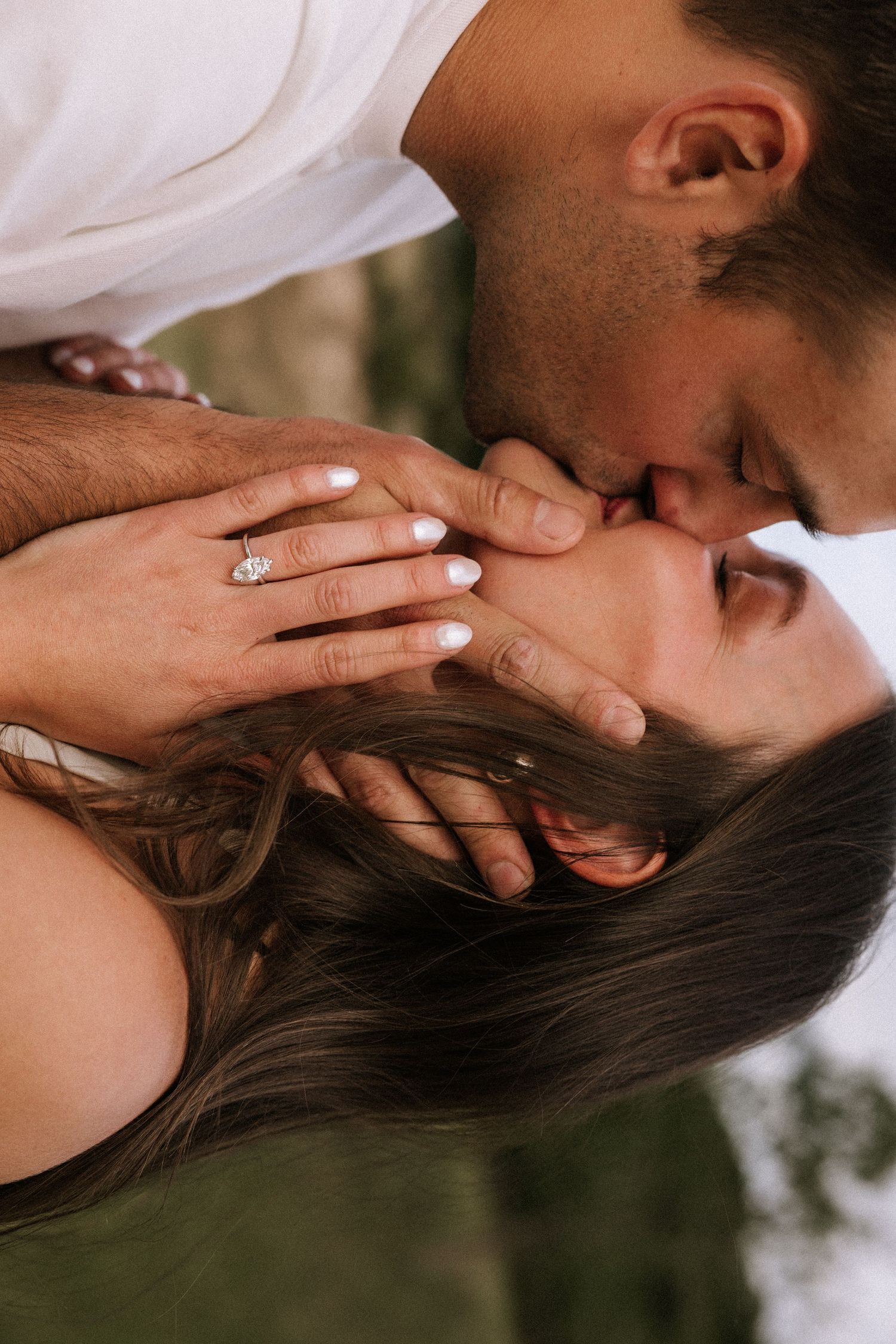 Couple sharing a romantic kiss with engagement ring visible on woman's hand during intimate photo session.