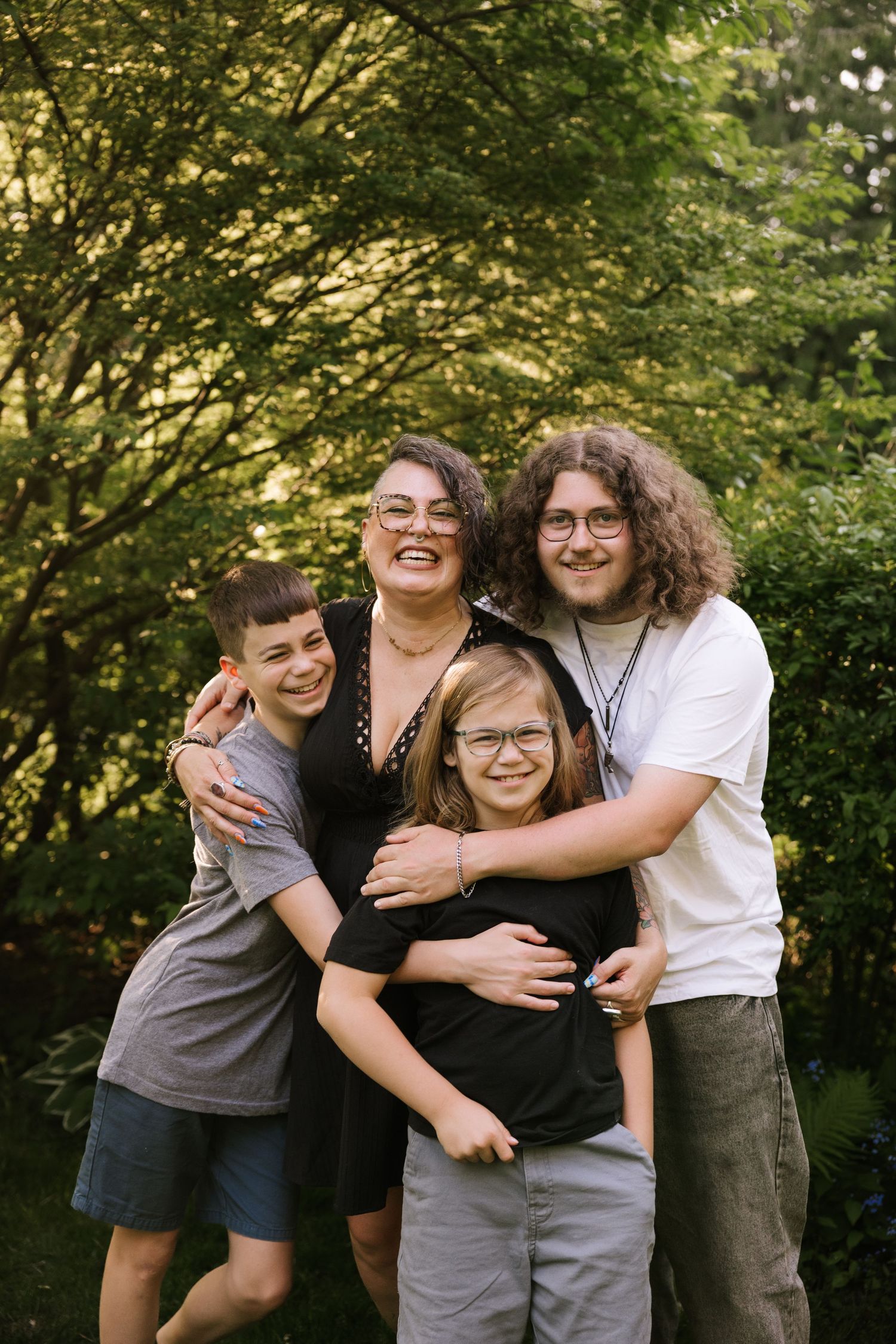 Laughing family group hug outdoors with green foliage background in warm natural light.