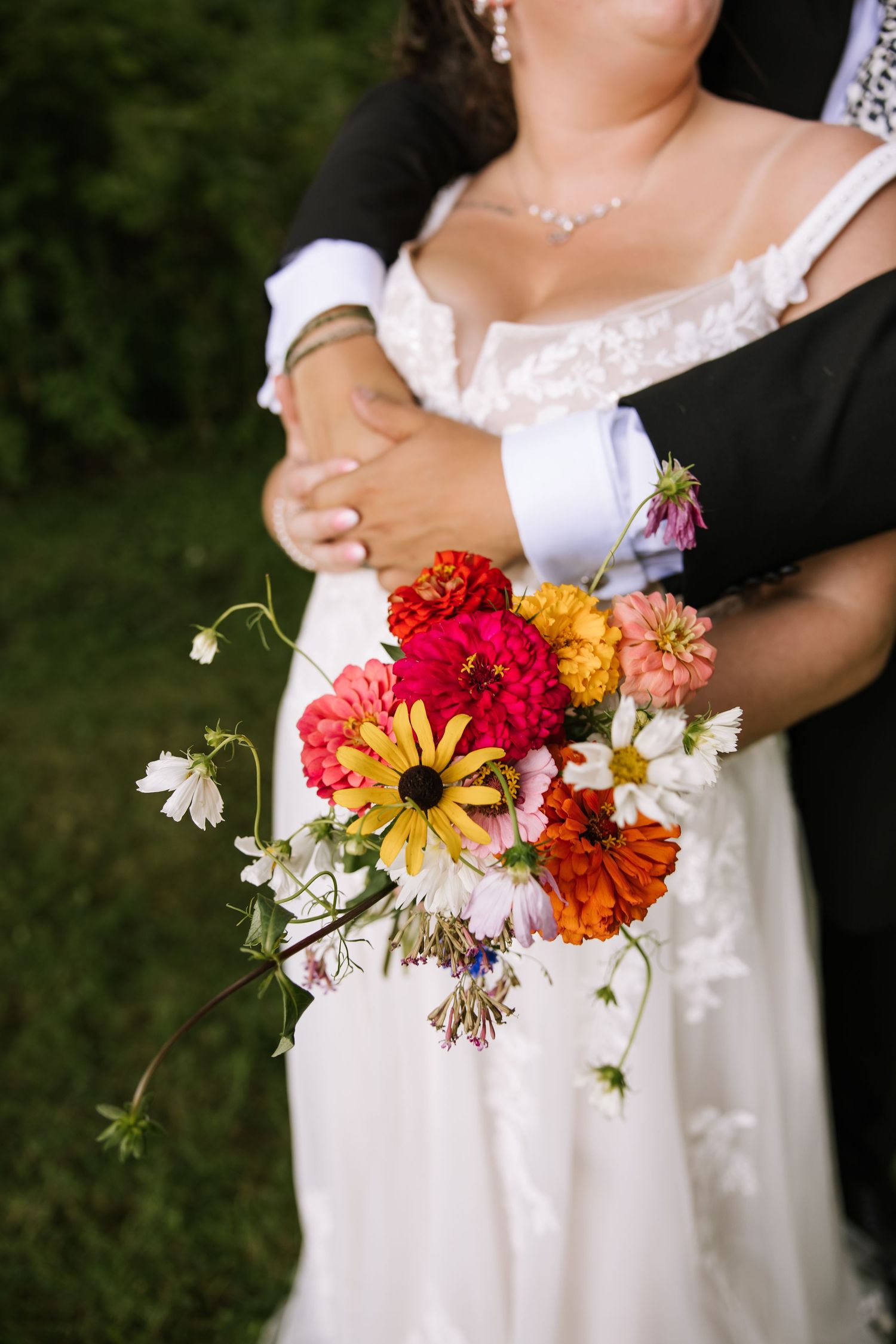 Colorful wildflower wedding bouquet with orange, red and yellow blooms held against a white dress.