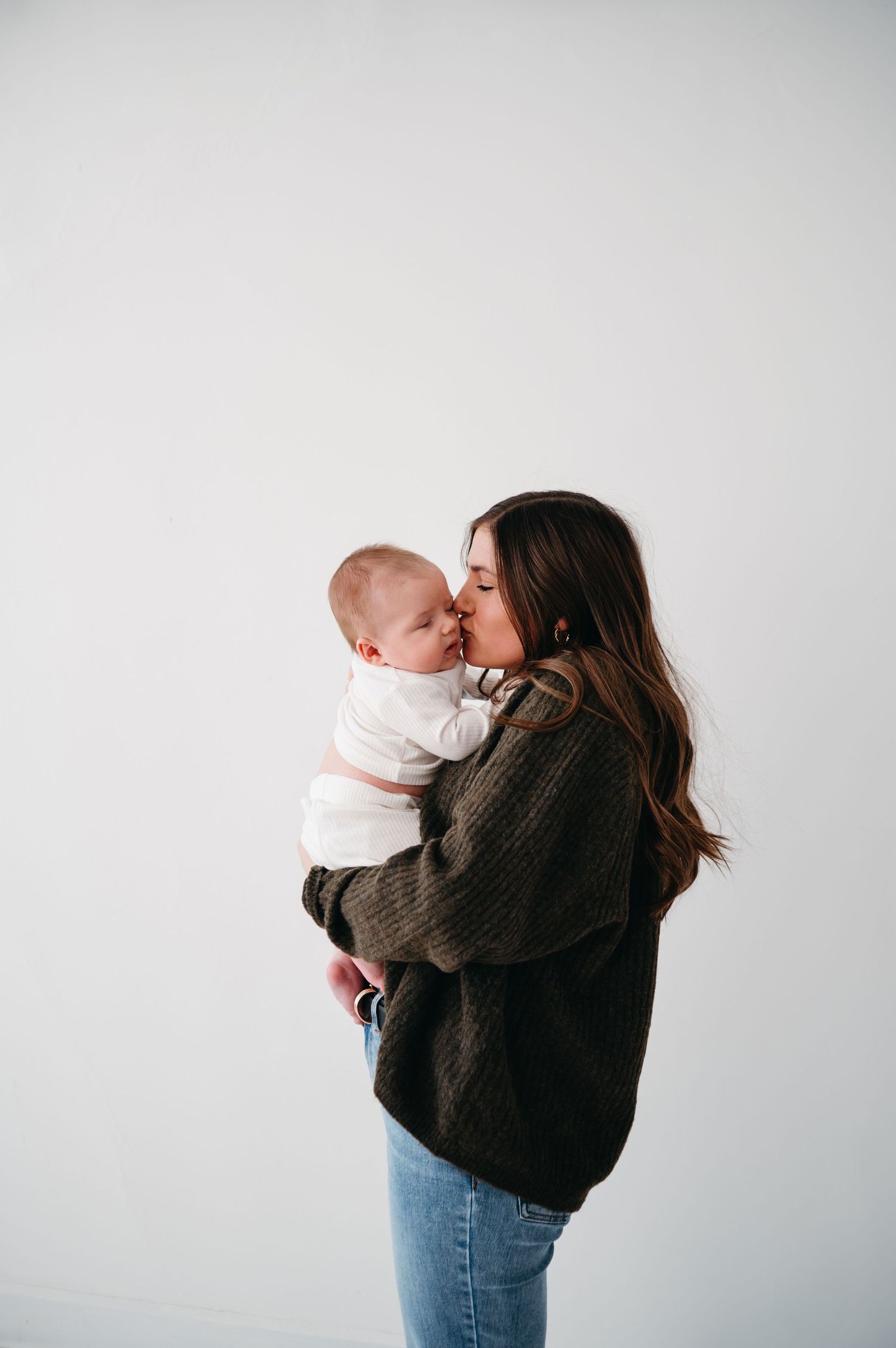 A tender moment between mother and baby as they cuddle in front of a white backdrop.