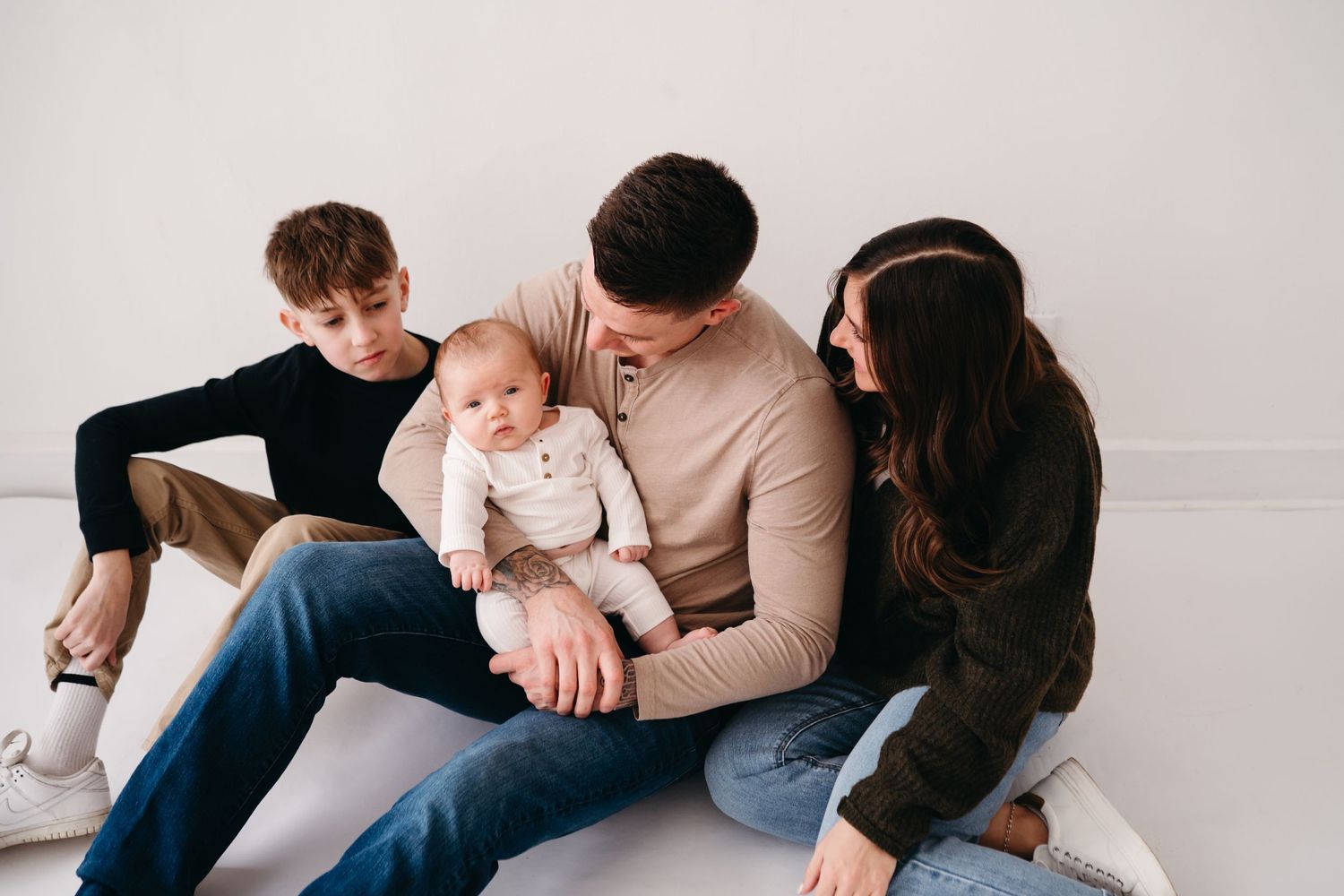 A family of four sitting closely together on the floor for an intimate portrait session.