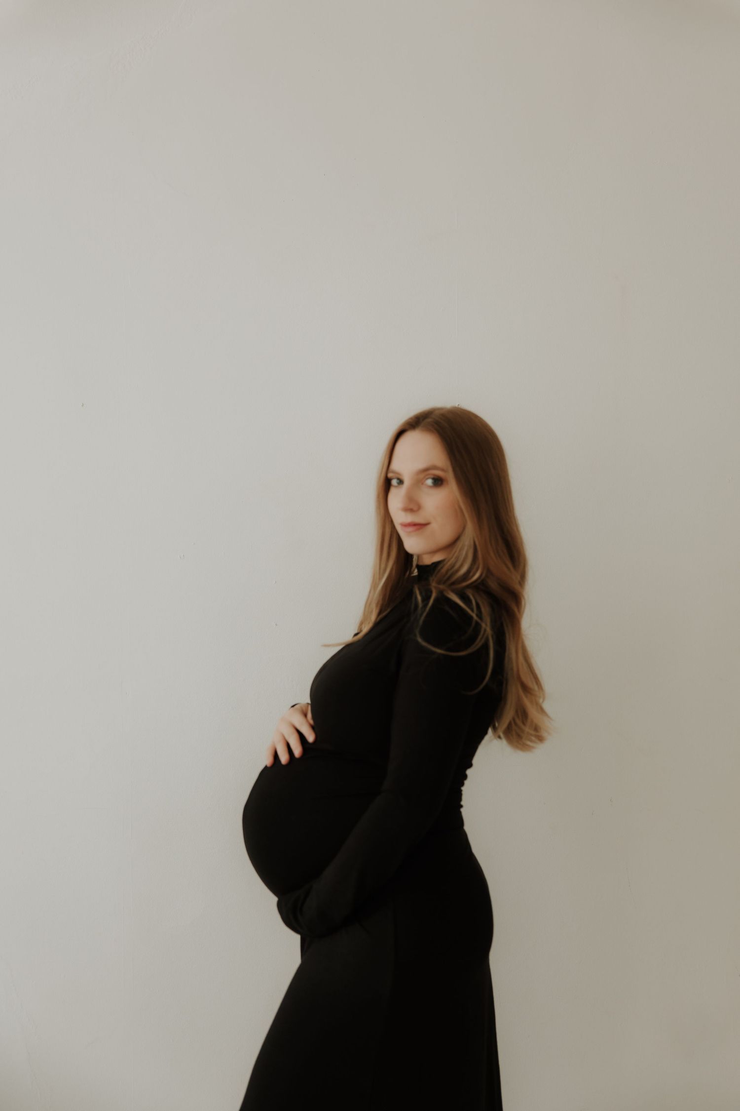 Elegant maternity silhouette in black dress against white backdrop.
