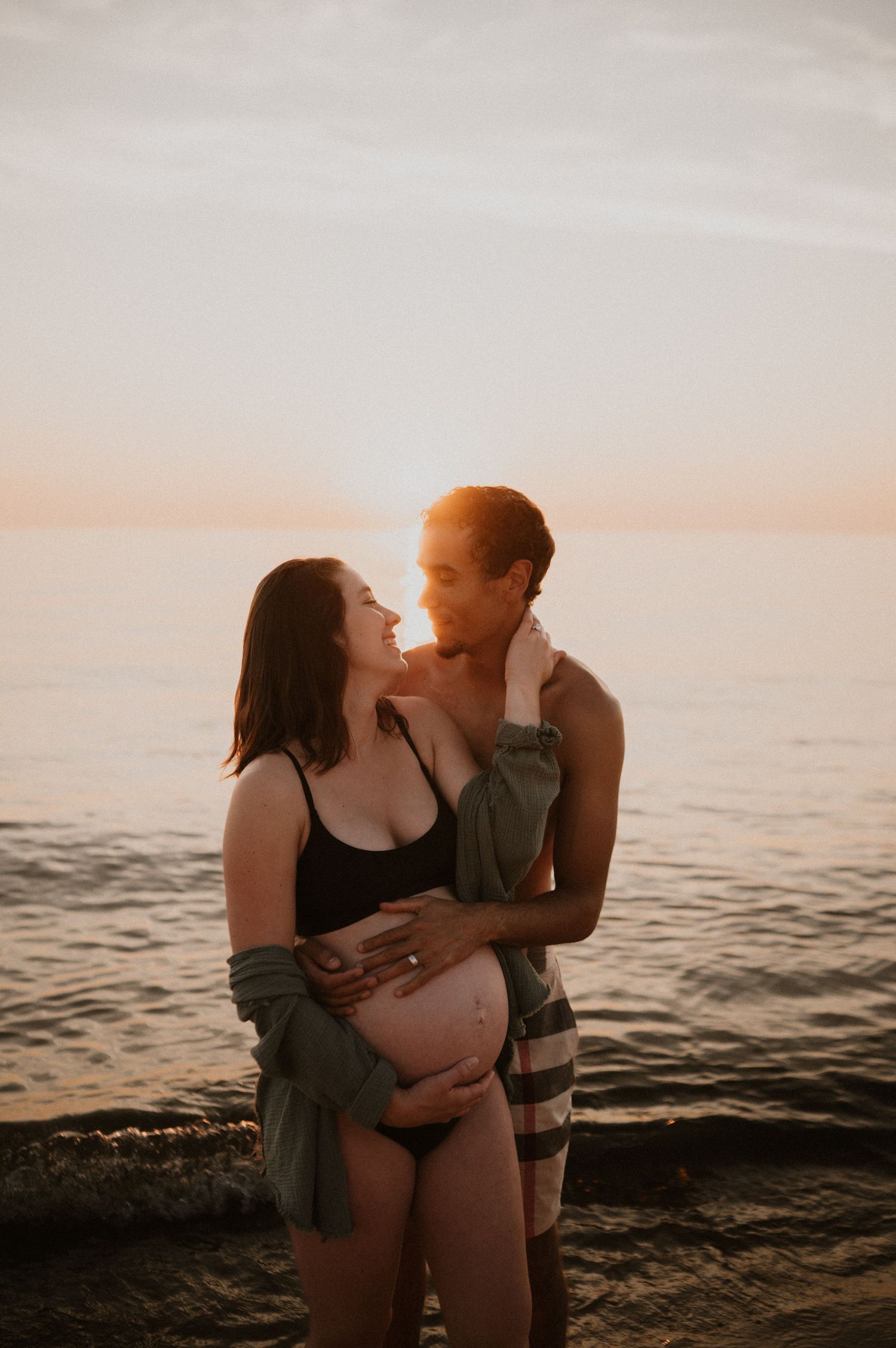 Maternity beach photo with couple sharing intimate moment at sunset.