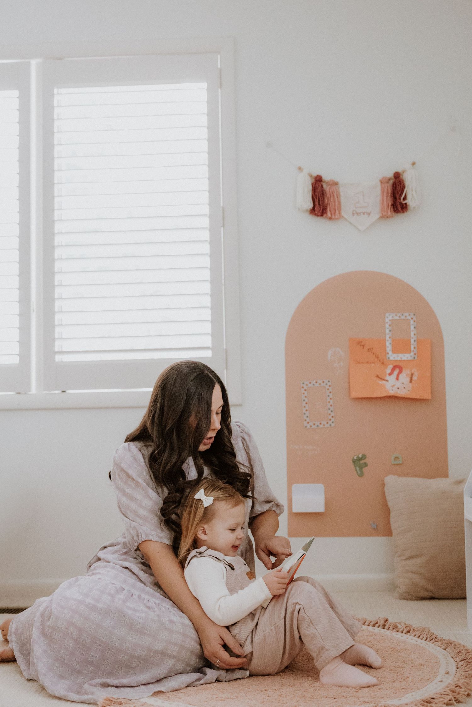A peaceful moment in a minimalist nursery with peach arch wall decor and white blinds.
