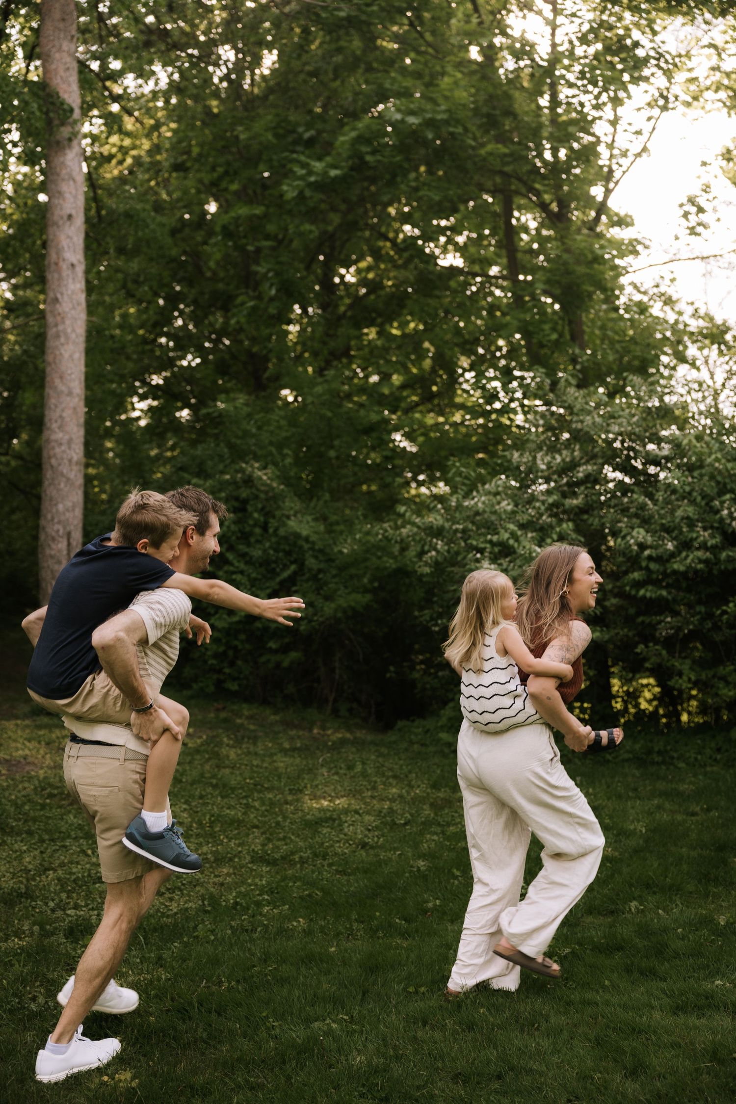 Two adults give children piggyback rides while playing in a lush green backyard.