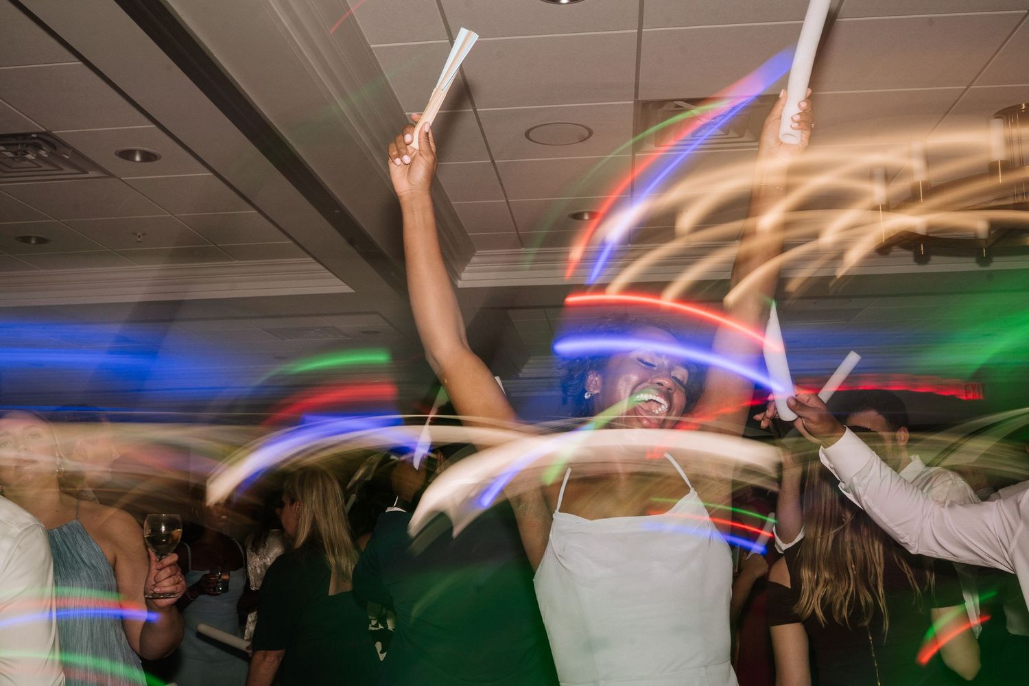 Blurred motion photo of wedding reception dancing with colorful lights creating streaks across the ceiling.