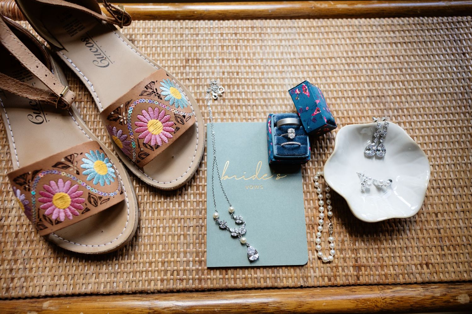 Wedding details including sandals, jewelry, and decorative items arranged on a woven surface.