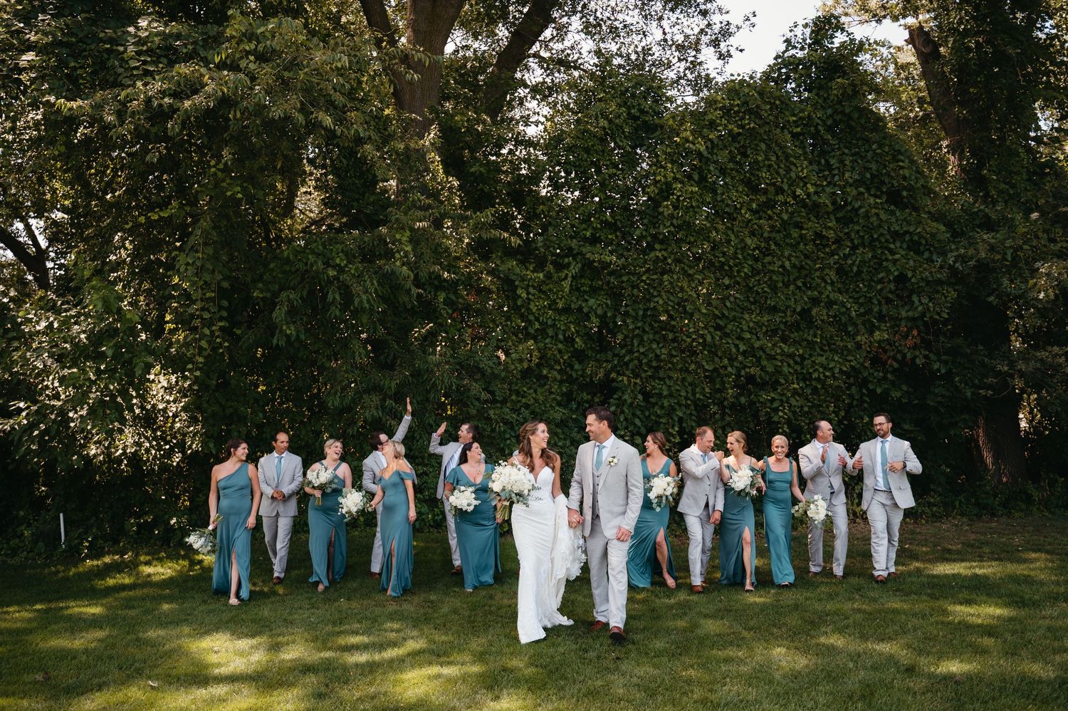 Wedding party in blue and white attire posed against a backdrop of trees.
