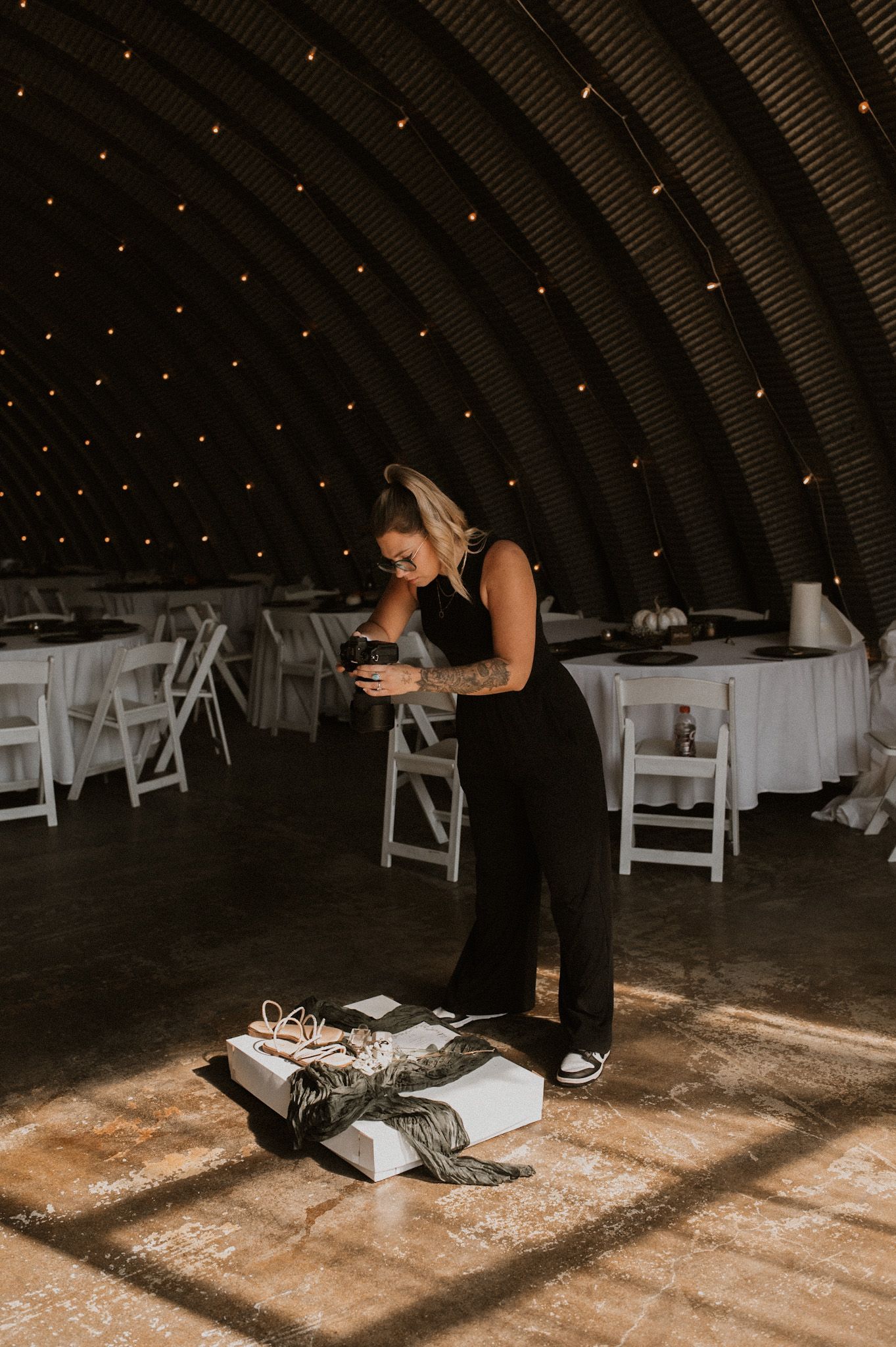Dark indoor barn venue with twinkle lights and white chairs being arranged.