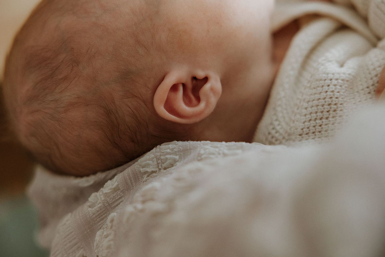 Close-up details of gentle hands cradling newborn baby.