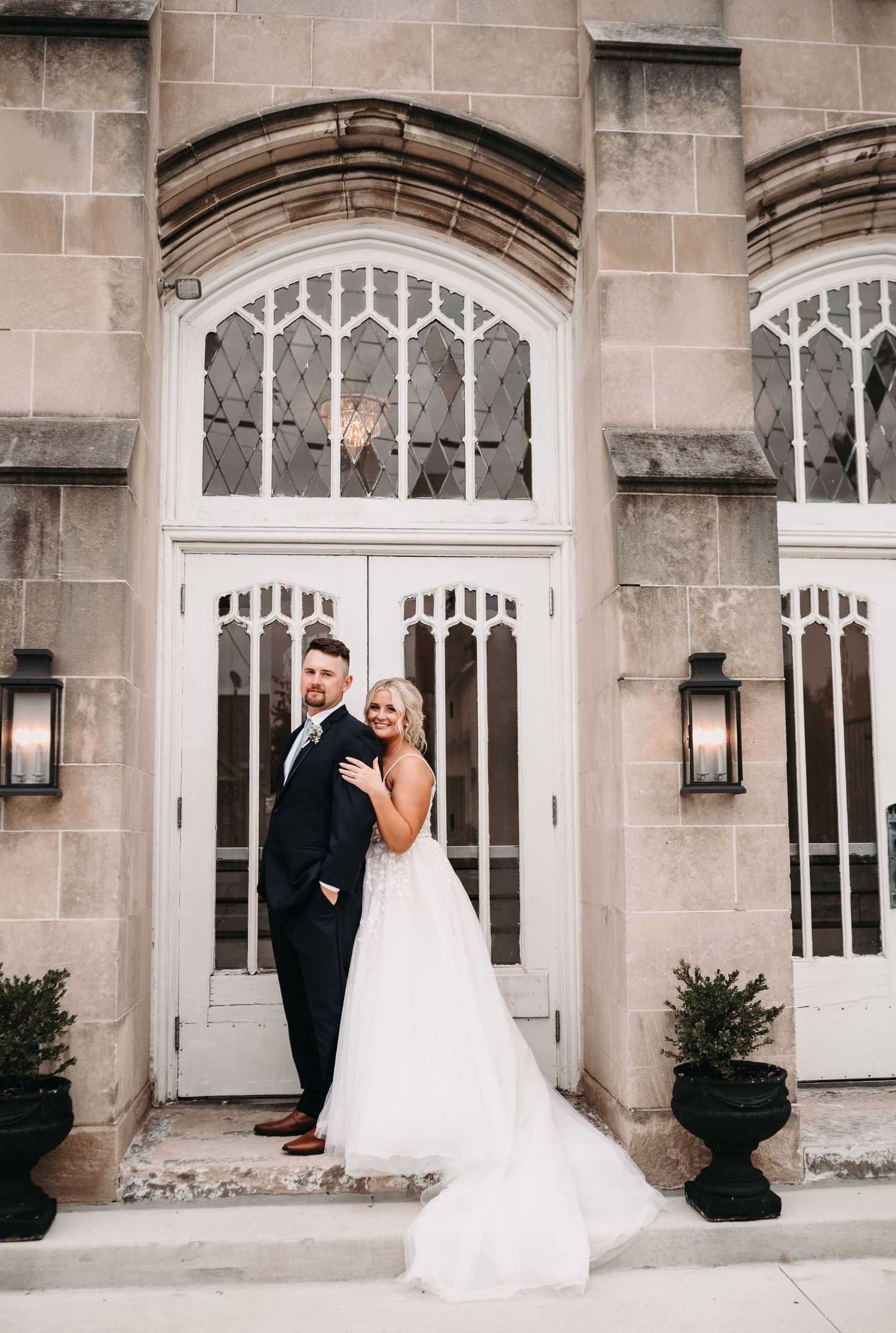 A wedding couple poses in front of an elegant Gothic-style doorway with white architectural details.