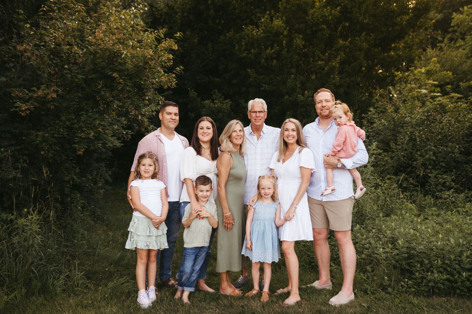Large multi-generational family group wearing coordinated outfits poses together in a garden setting.