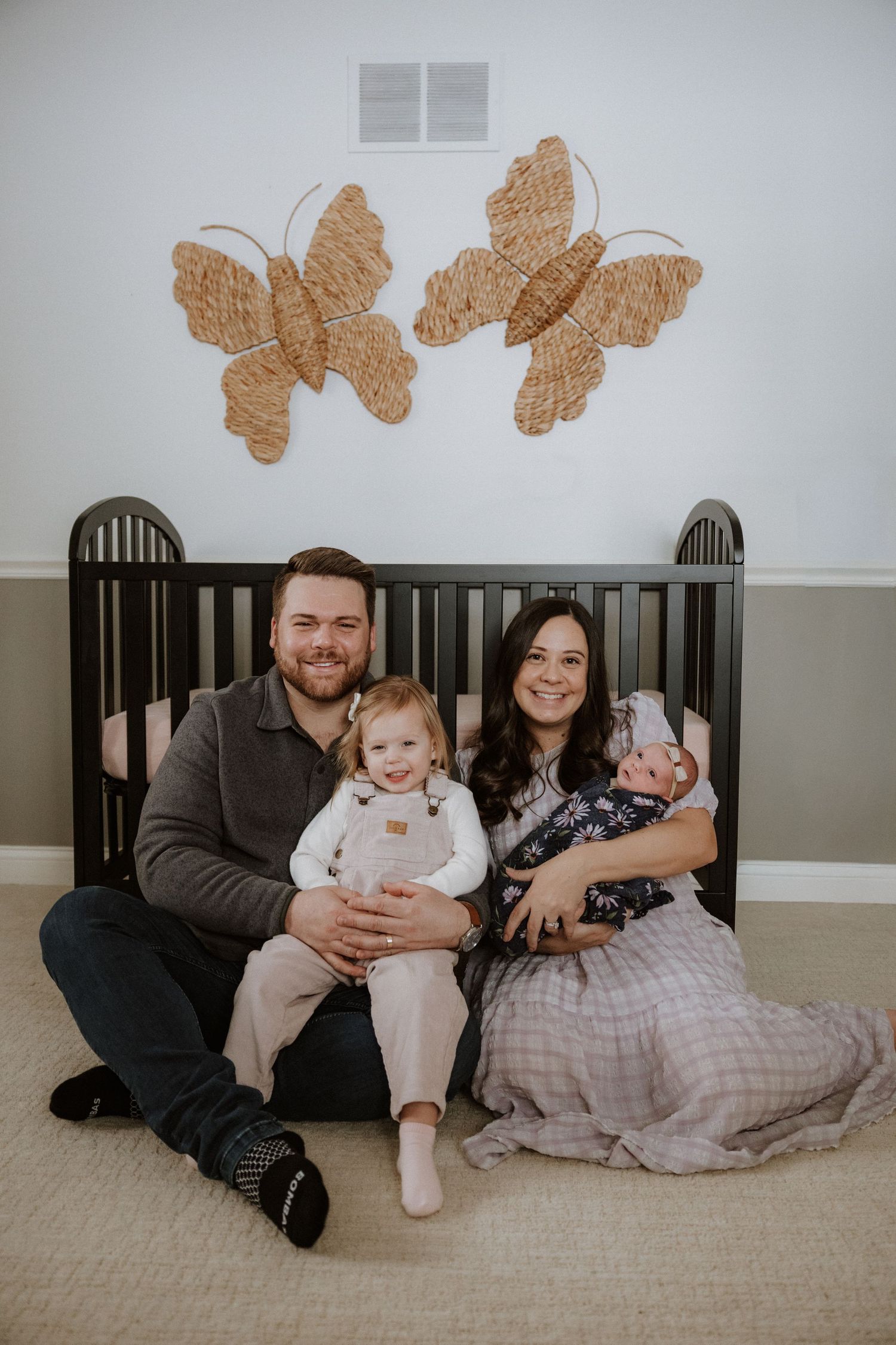 Family sitting together against a black crib with butterfly decorations on the wall.