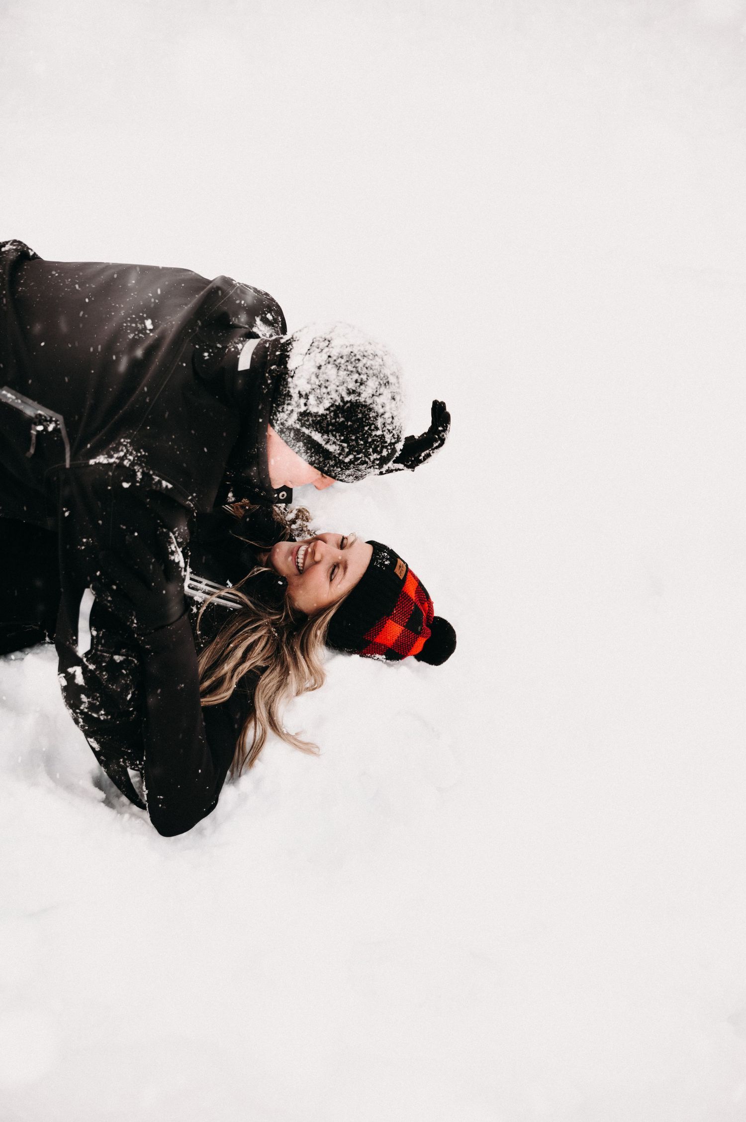Two people in winter gear playing in the snow with snowflakes falling around them.