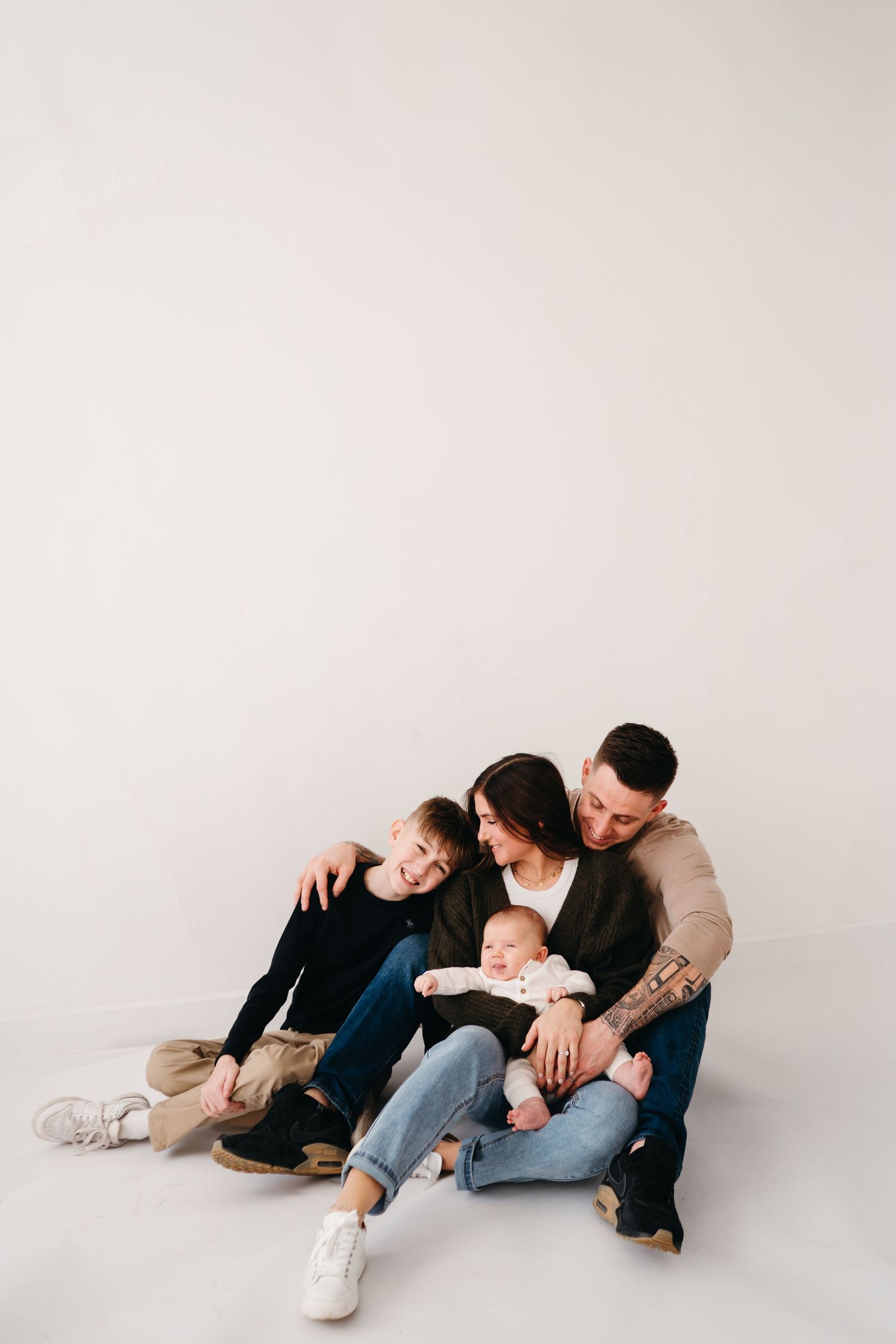 A family sits together on a white floor in a studio, sharing a relaxed and playful moment.