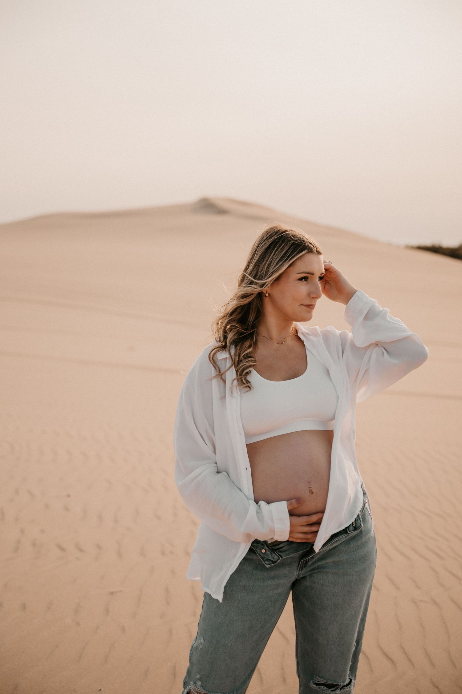 Expectant mother in casual wear poses thoughtfully against desert landscape.