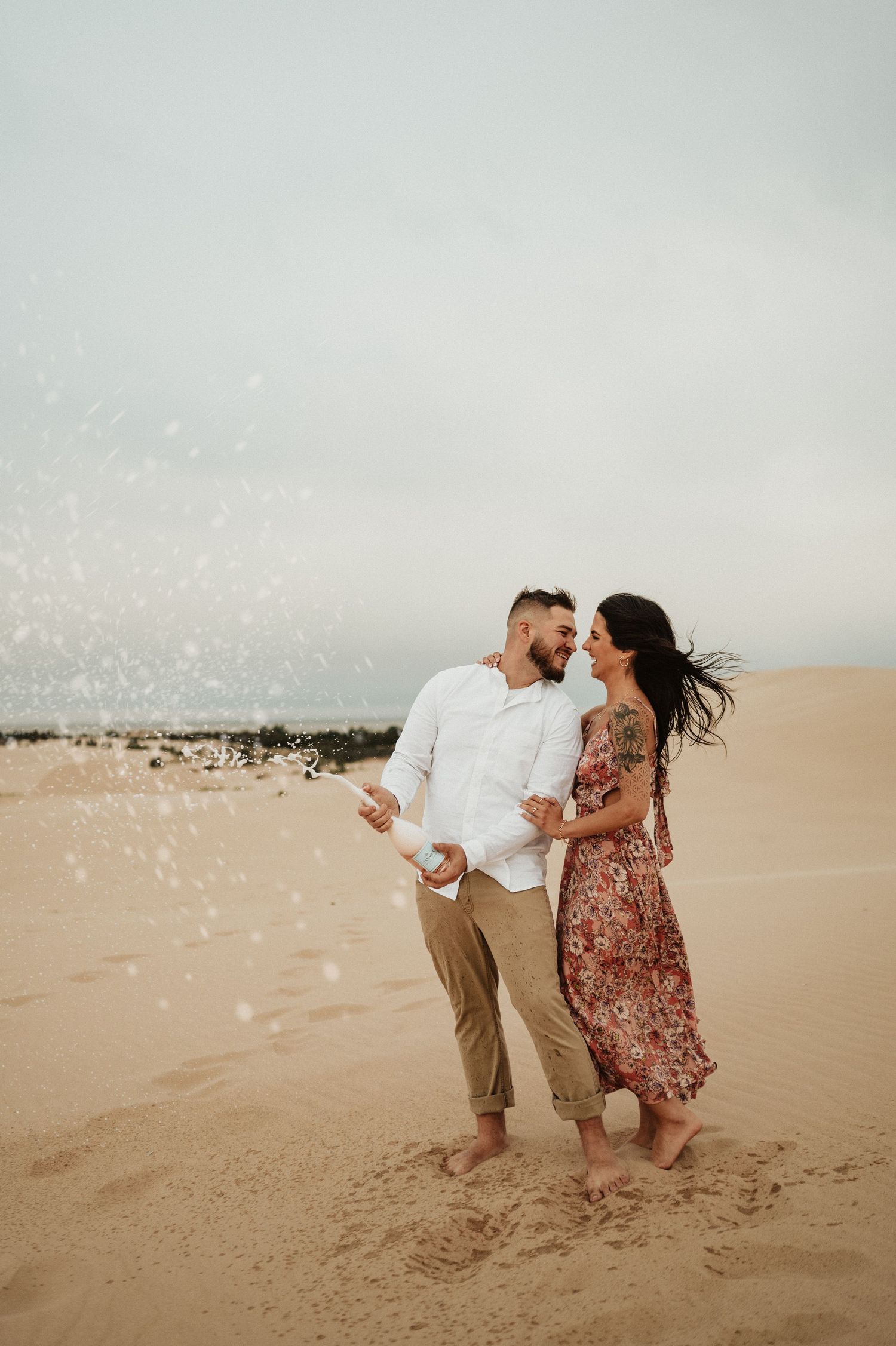 A couple shares a romantic moment on sand dunes with sparkles in the foreground.