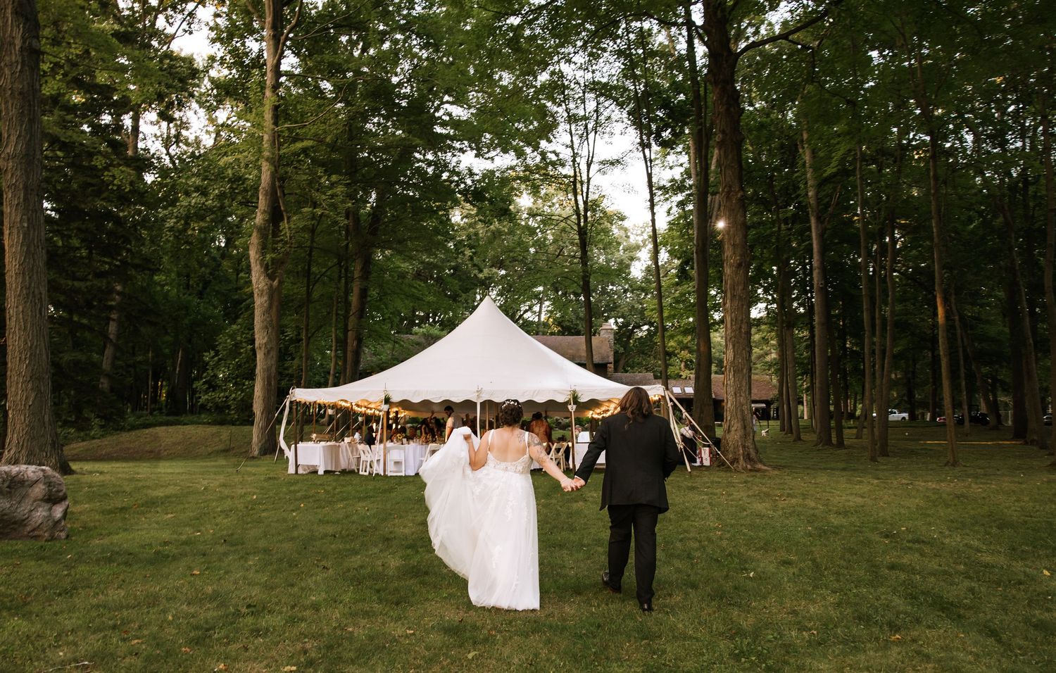 A scenic outdoor event space with white tents set up among tall trees at dusk.